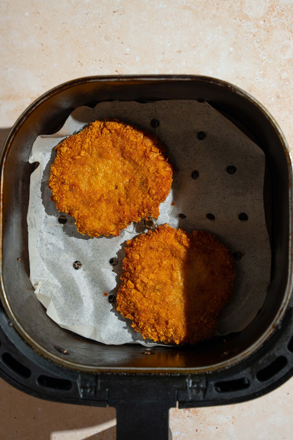 An air fryer tray lined with parchment paper with two fried McChicken chicken patties. The tray is on a tan counter.