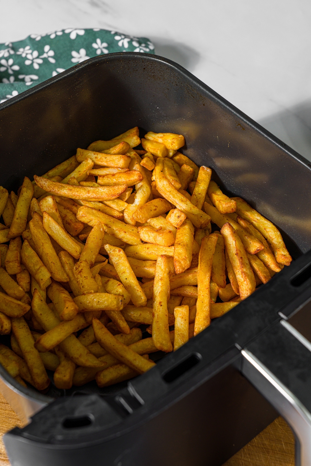 An air fryer tray with crispy fries. The tray is on a marble counter with a green floral napkin.