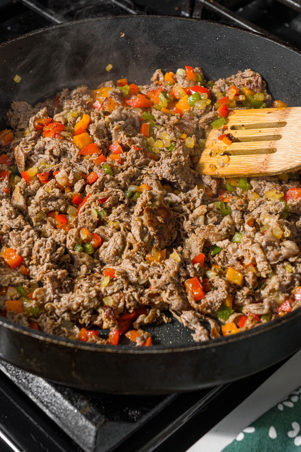 A skillet with a wooden spoon mixing a ground beef and pepper mixture. The skillet is cooking on the stove.