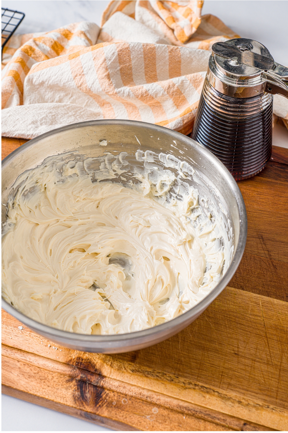 A large bowl of whipped frosting on a wooden board with a yellow striped napkin.