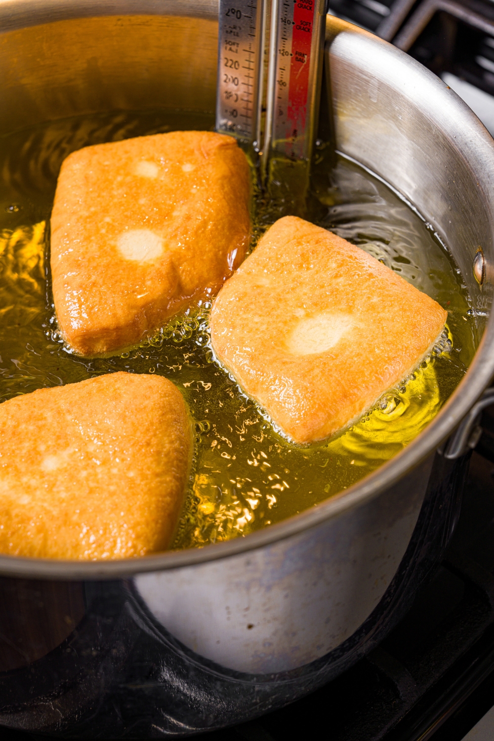 A pot of hot oil with several beignets frying in oil. The pot is cooking on the stove.