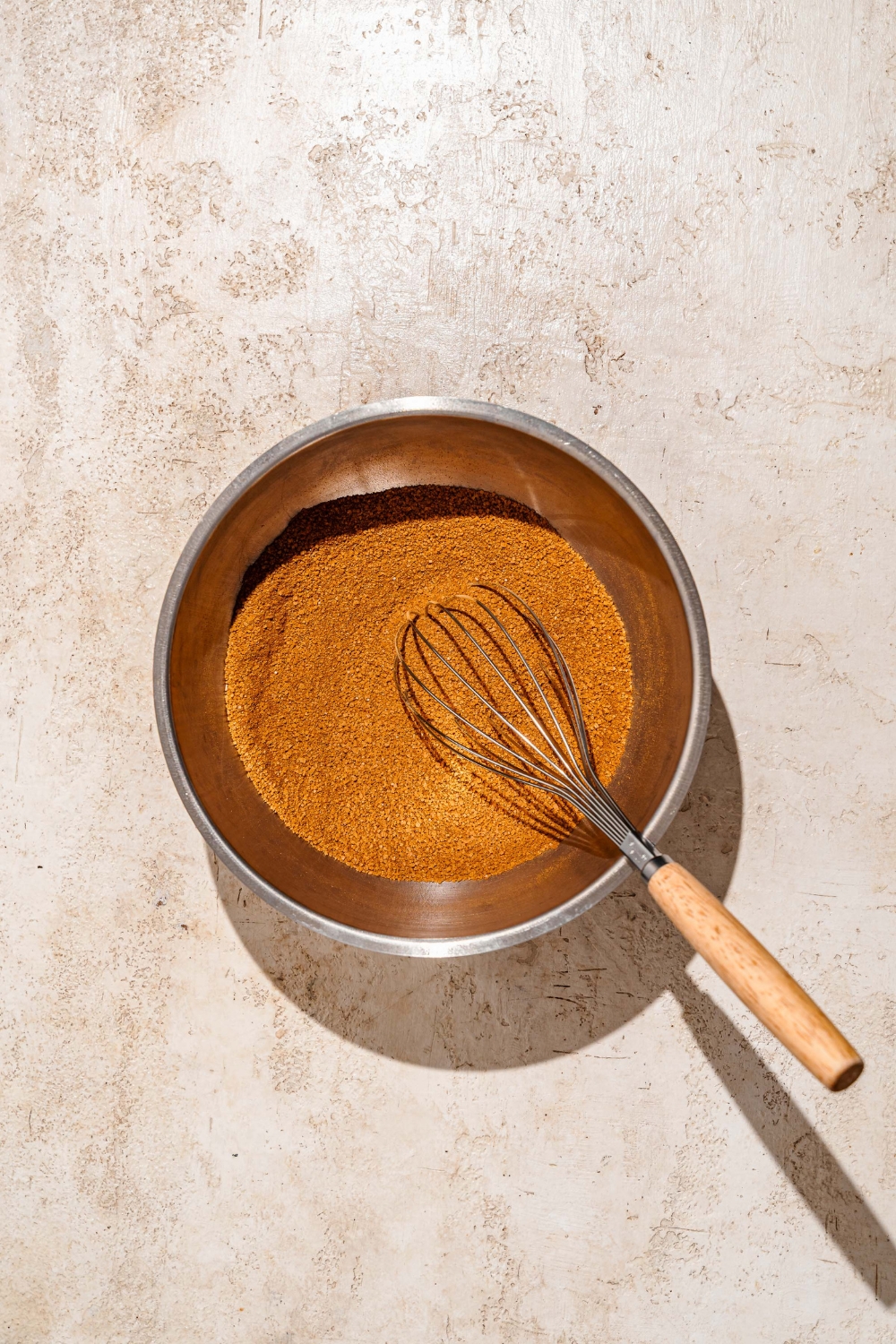 A mixing bowl with a whisk mixing a cinnamon mixture. The bowl is on a tan counter.