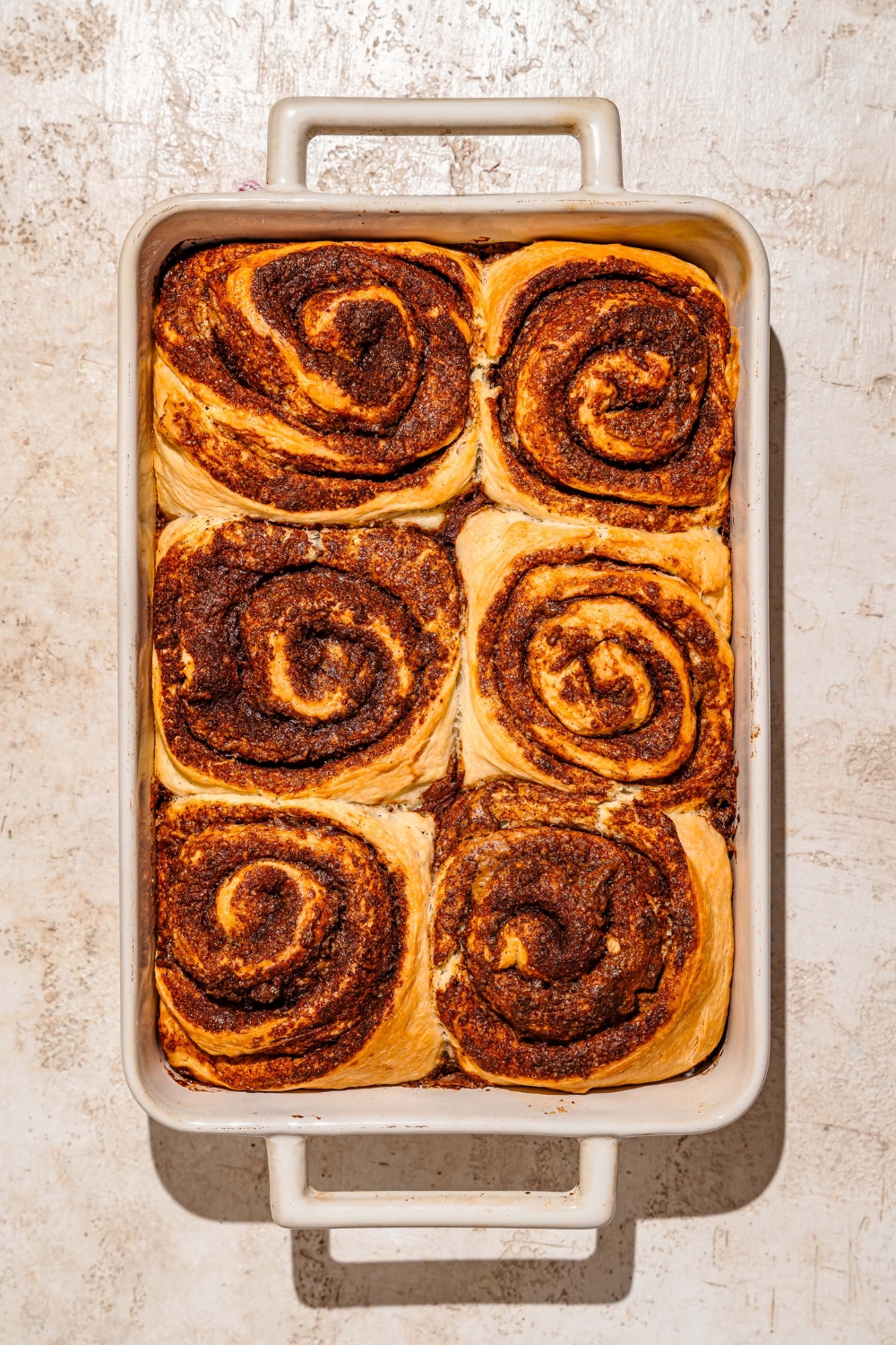 A baking pan with baked Biscoff cinnamon rolls. The pan is on a tan counter.