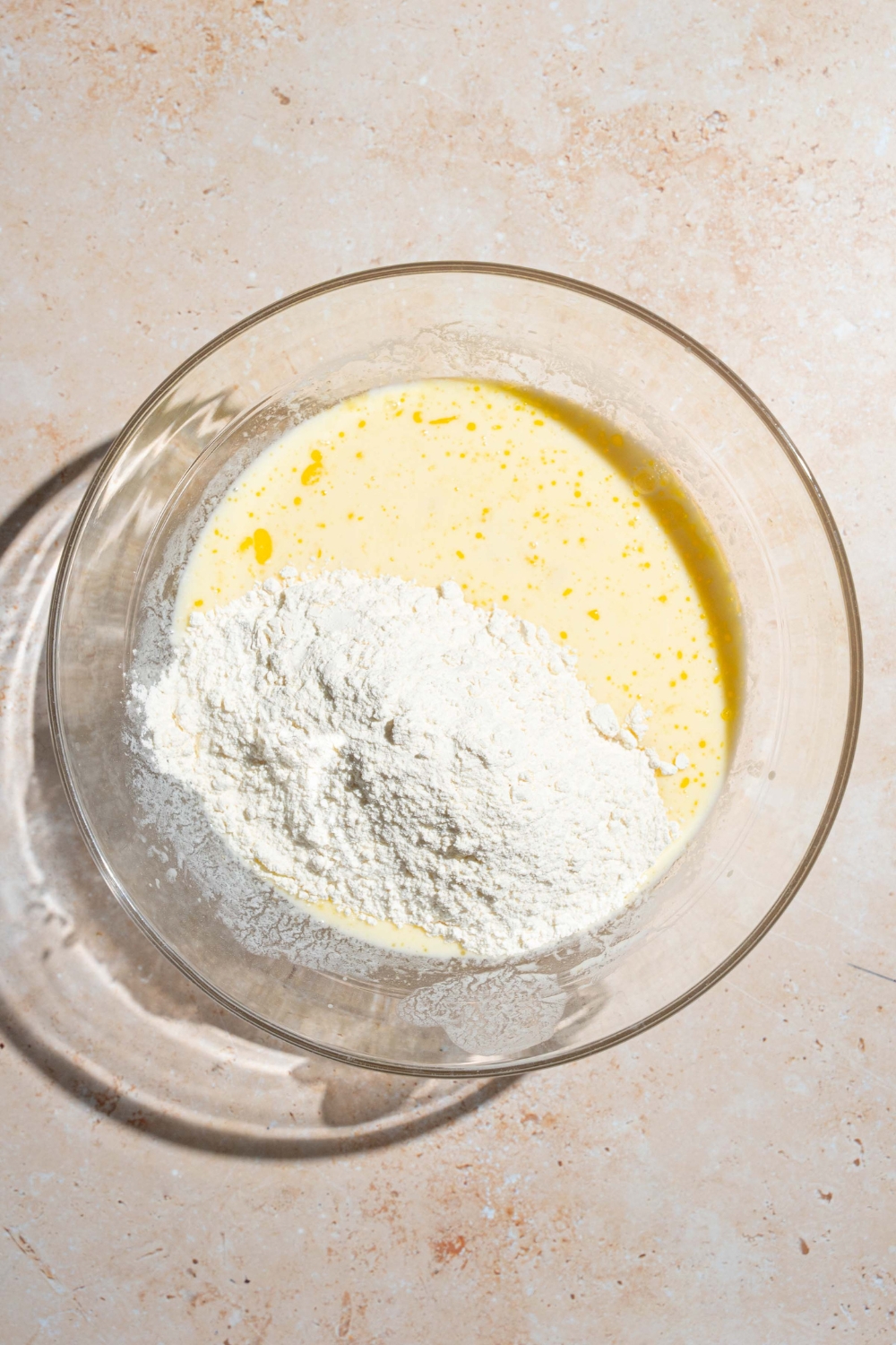 A large bowl with wet batter mixture topped dry ingredients. The bowl is on a tan counter.