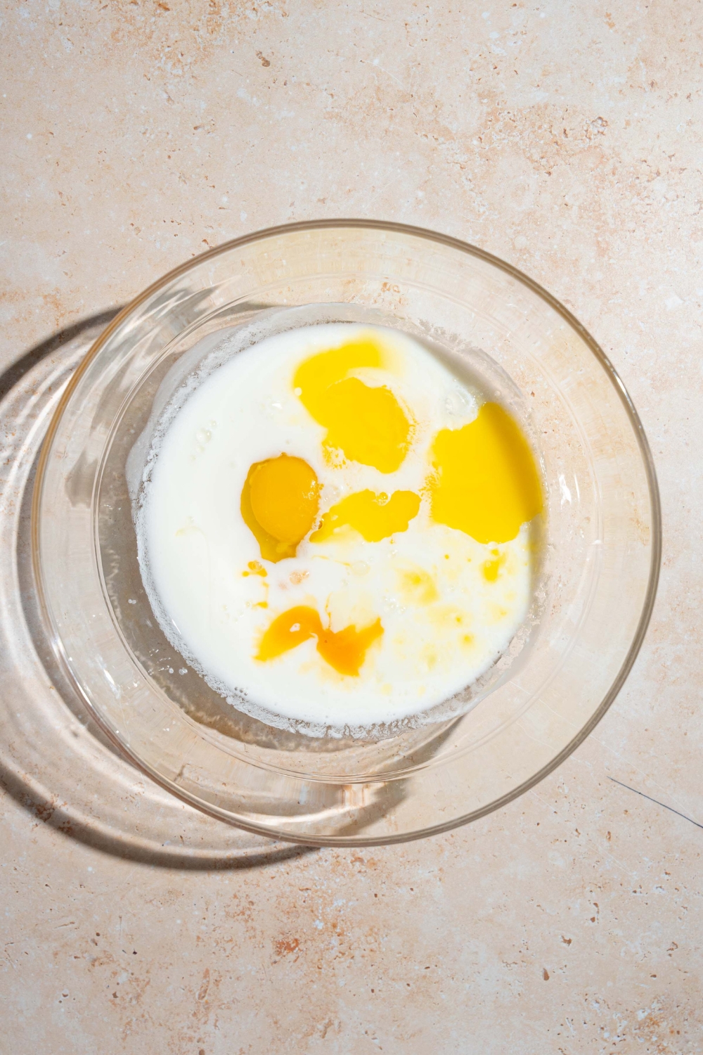 A large bowl with wet ingredients to make blueberry pancake batter including buttermilk, eggs, and vanilla. The bowl is on a tan counter.