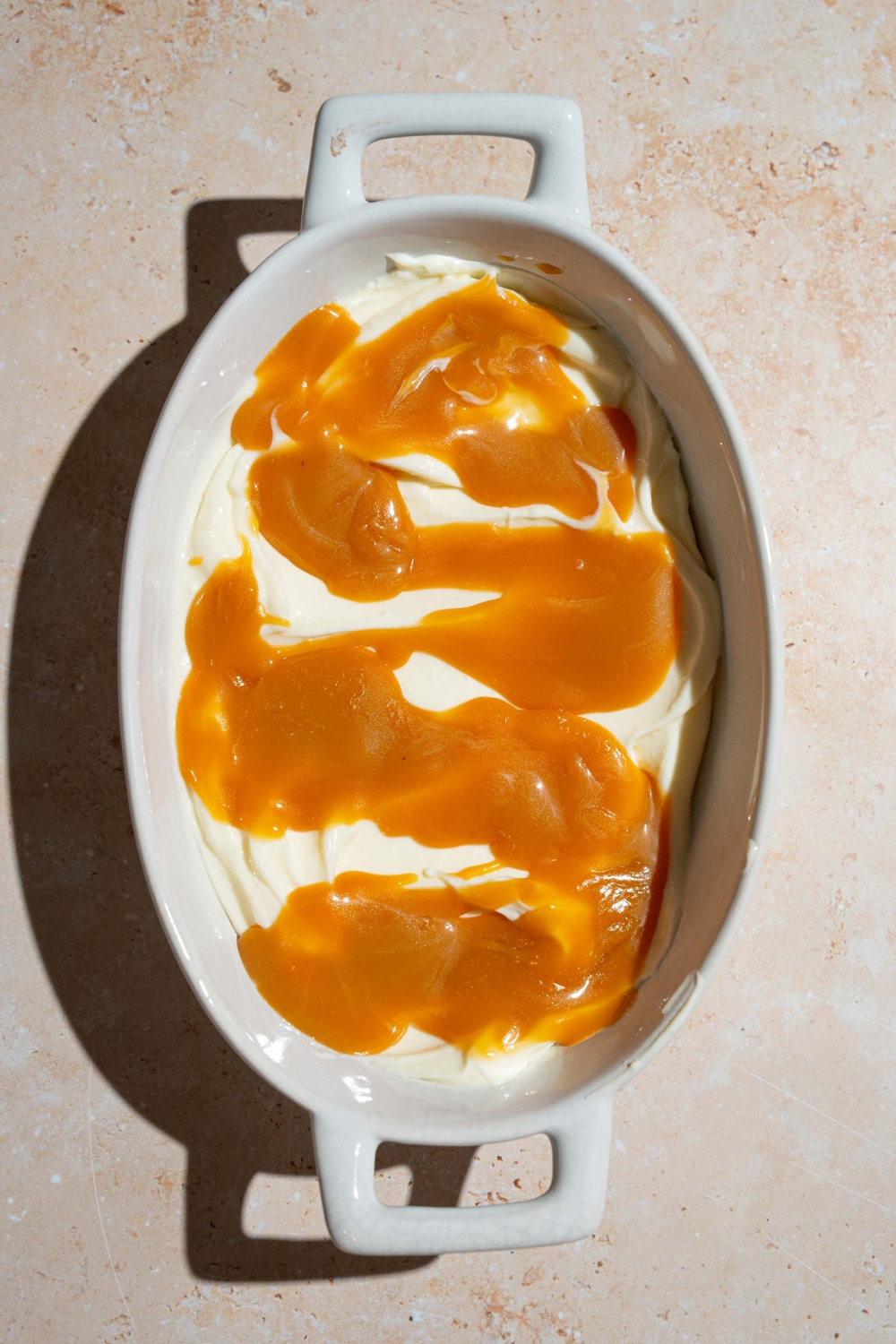 A platter covered with cheesecake filling layered with caramel sauce. The platter is on a tan counter.