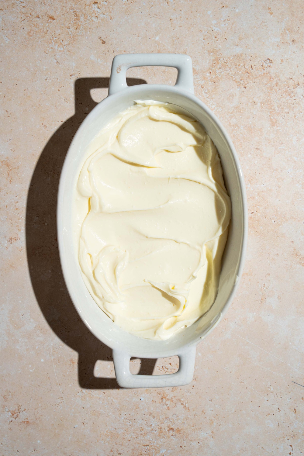 An oval player covered in cheesecake filling. The platter is on a tan counter.