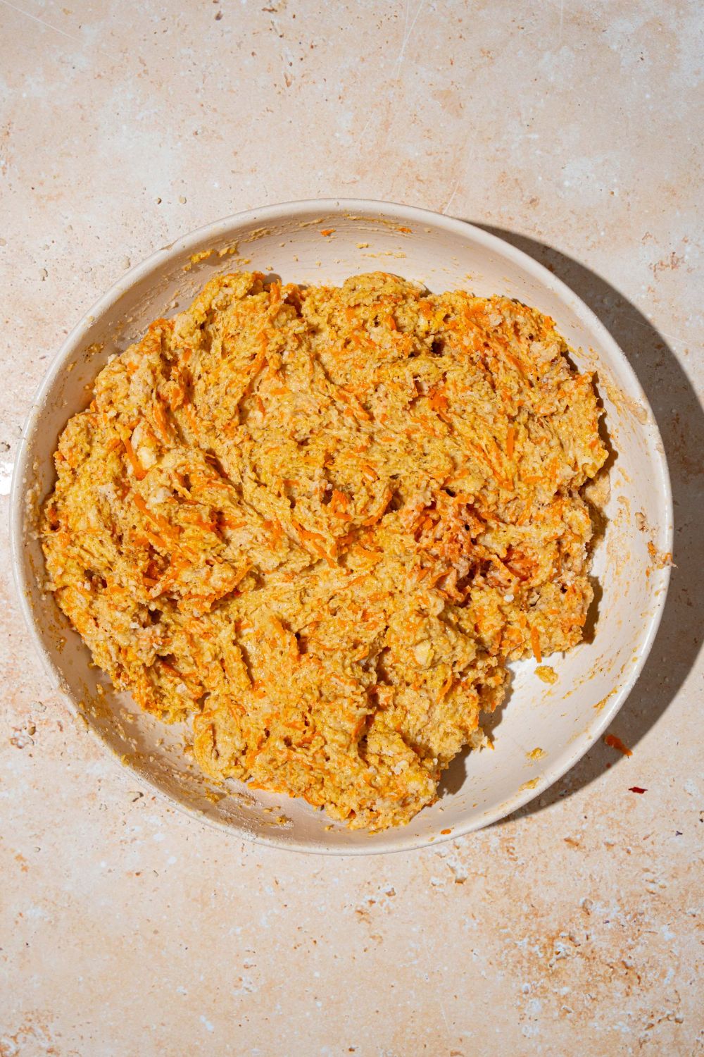 A large bowl with a carrot cake cobbler dough mixture. The bowl is on a tan counter.