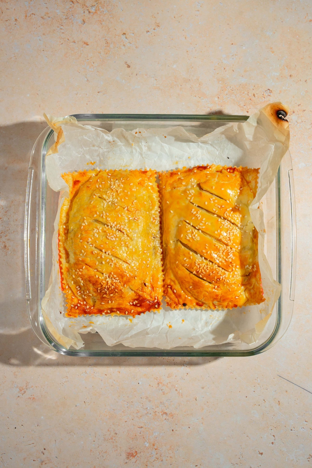 A glass baking dish lined with parchment paper with two baked cheeseburger hot pockets. The dish is on a tan counter.