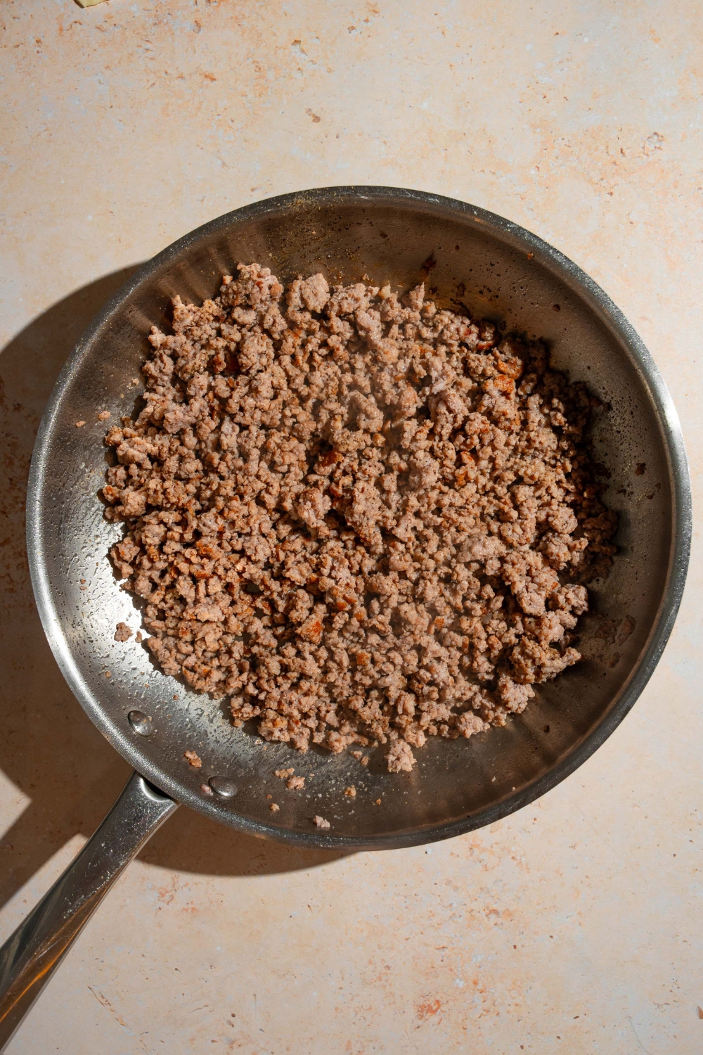 A skillet with ground beef. The skillet is on a tan counter.