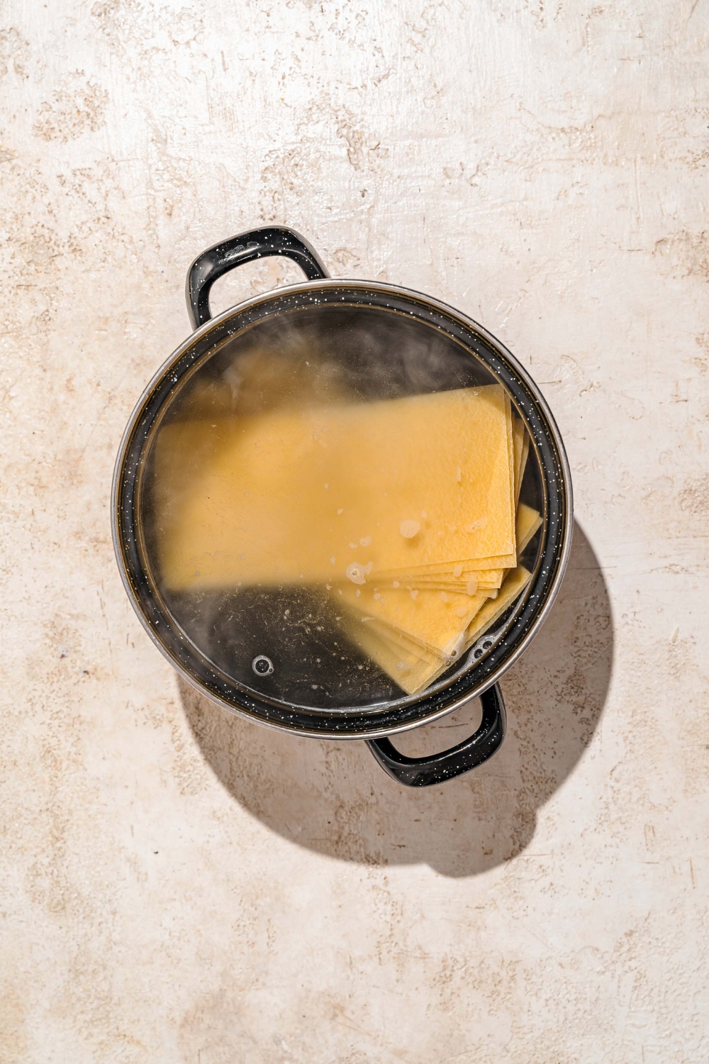 A large bot of water with lasagna noodles soaking in the pot. The pot is on a tan counter.