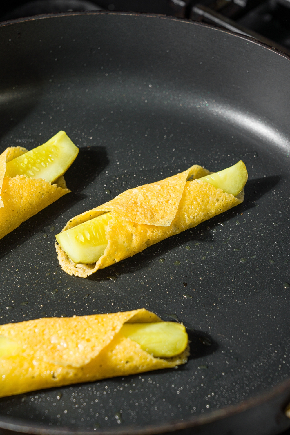 A skillet with pickles wrapped in cooked slices of gouda cheese.