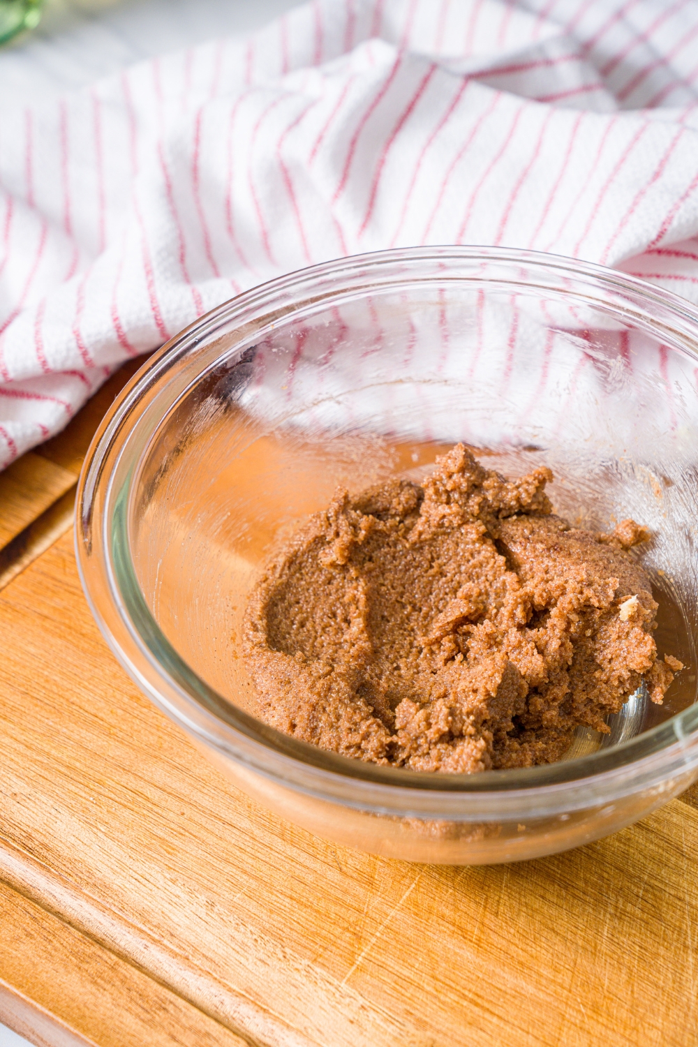 A glass bowl with a cinnamon sugar mixture. The bowl is on a wooden board with a red striped napkin.