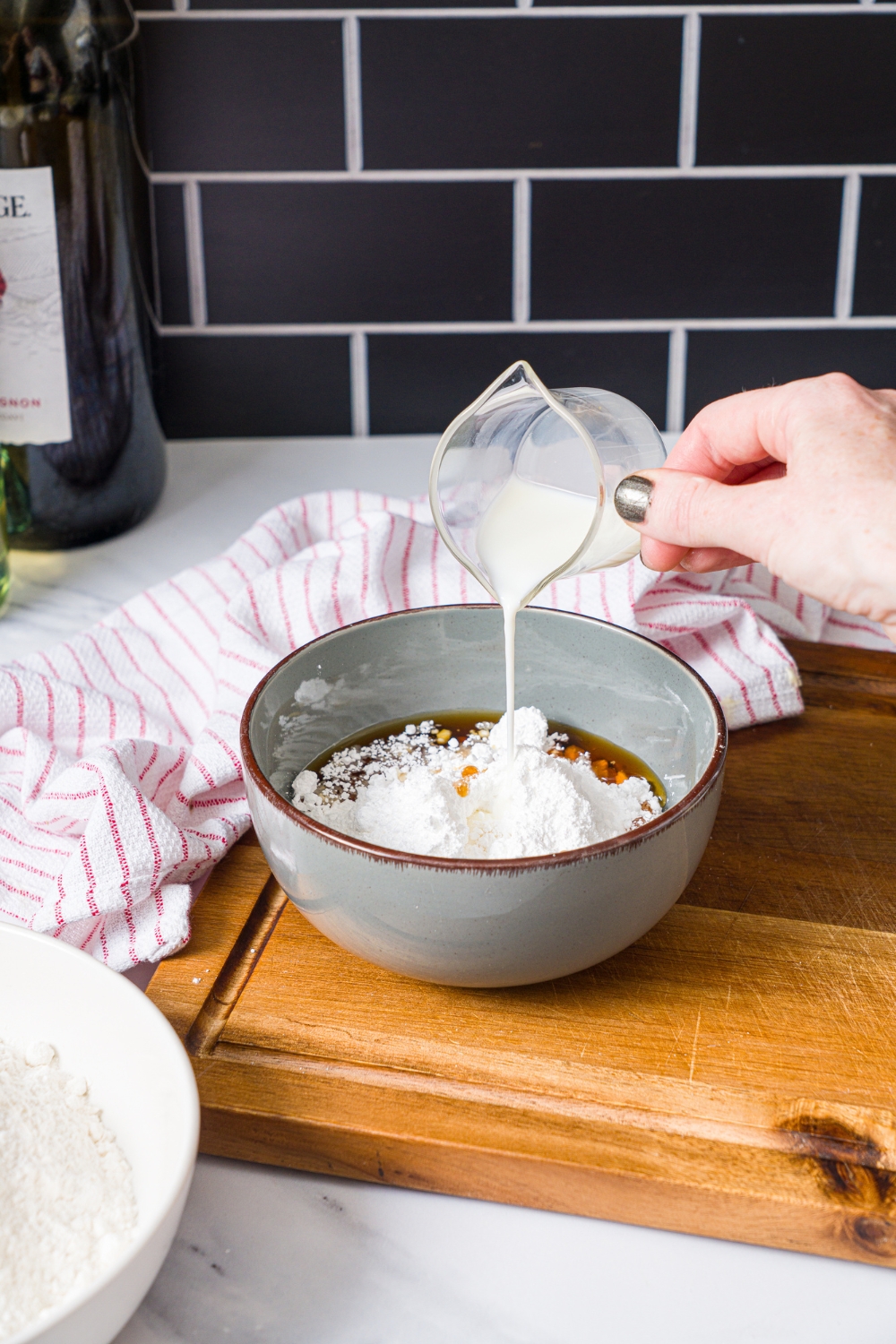 A bowl of ingredients to make cinnamon glaze with milk being poured into the mixture. The bowl is on a wooden board with a red striped napkin.