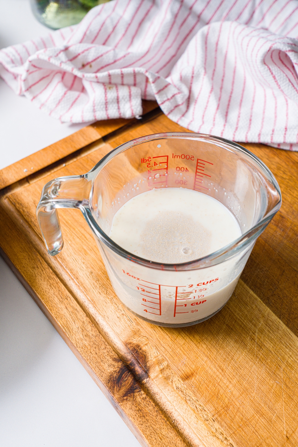 A measuring cup with a yeast mixture. The cup is on a wooden board with a red striped napkin.