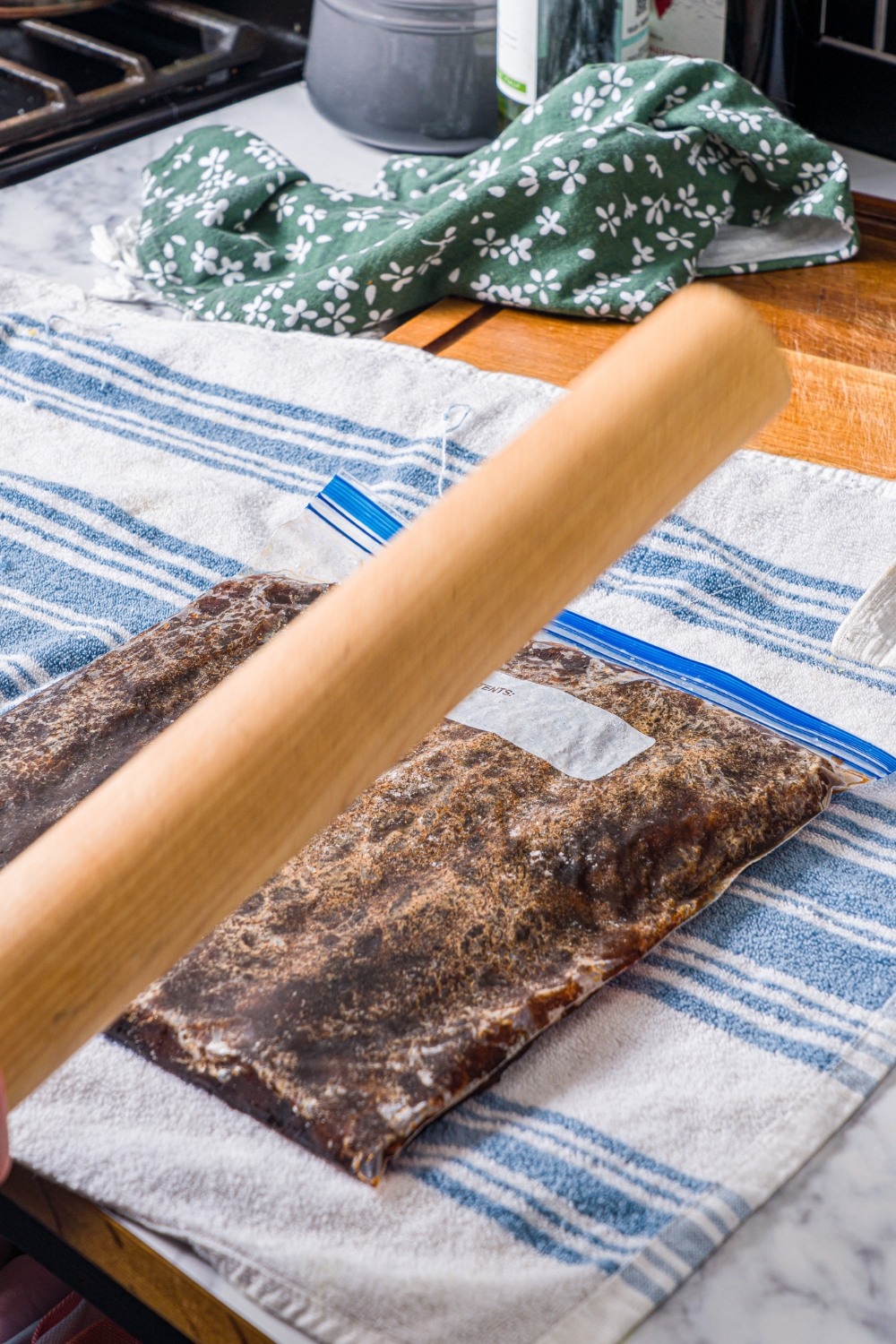 A freezer bag with frozen coffee on a dish cloth with a rolling pin crushing the bag.