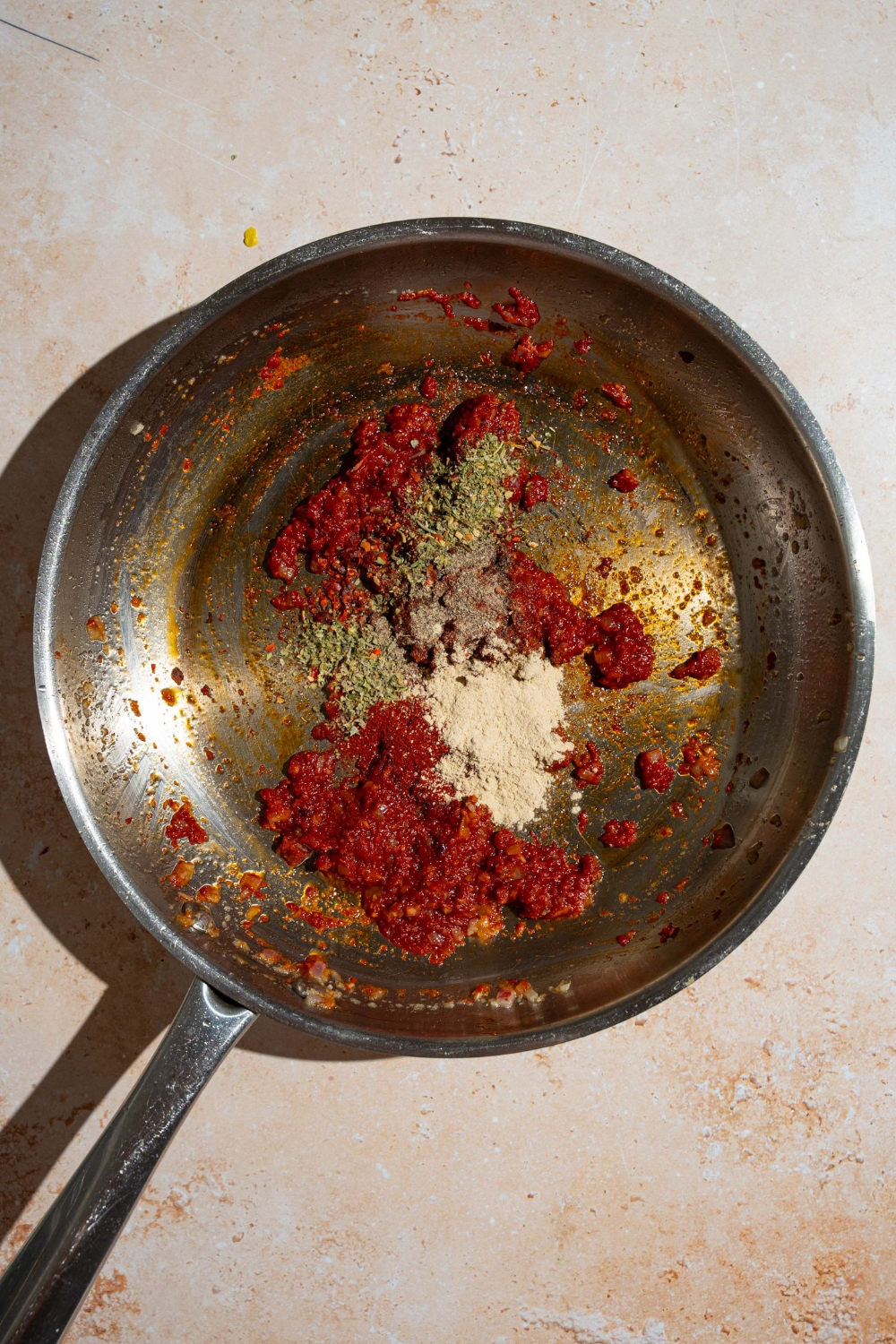 A skillet with tomato paste and seasonings. The skillet is on a tan counter.