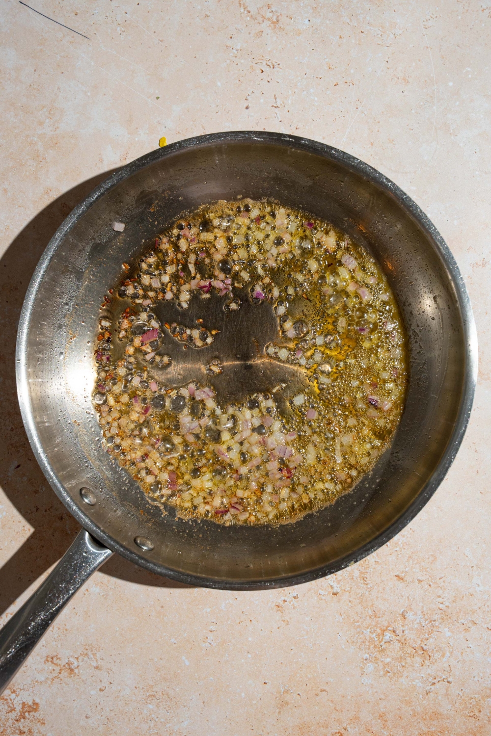 A skillet with red onion and garlic sautéing in oil. The skillet is on a tan counter.