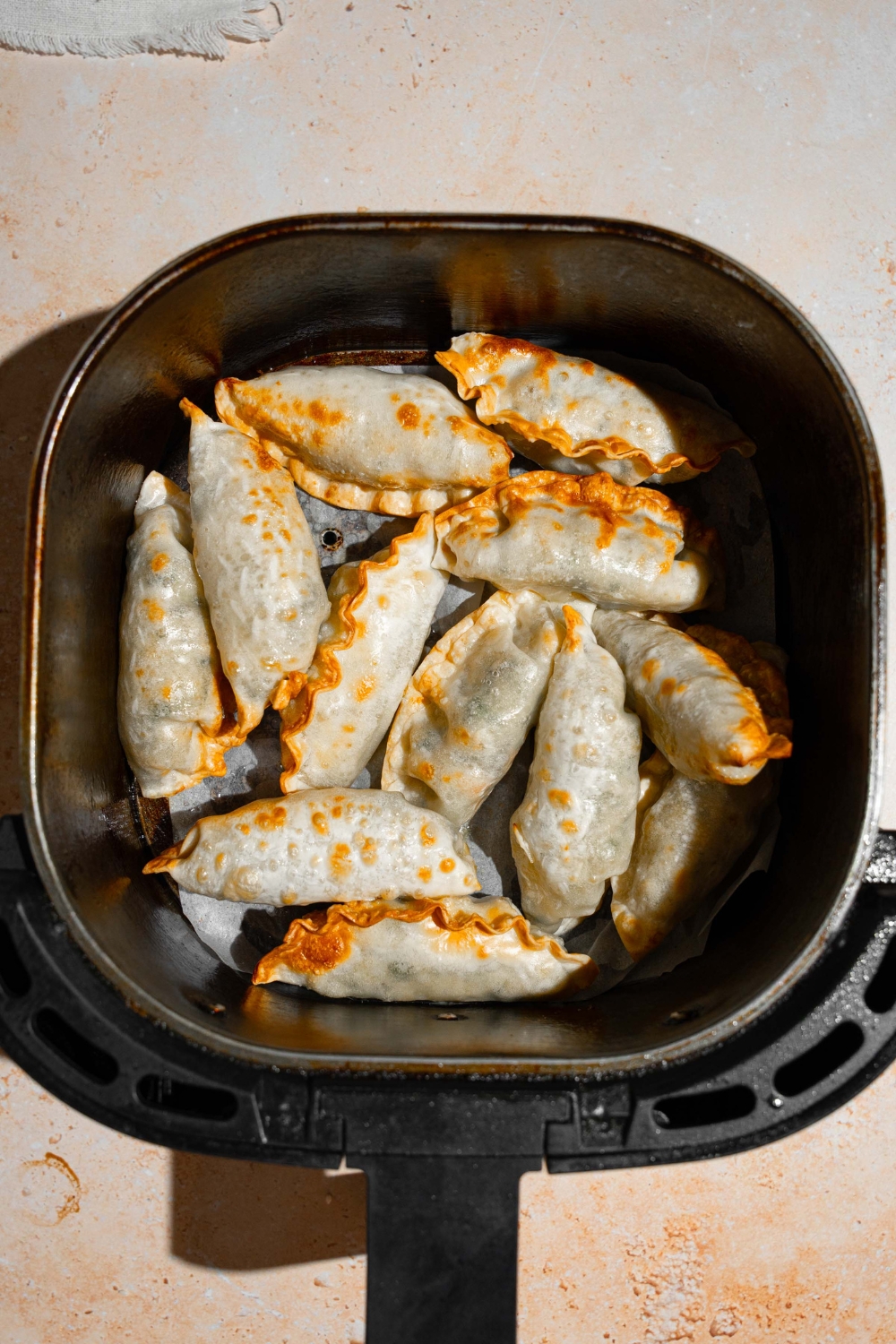 An air fryer basket with fried dumplings. The basket is on a tan counter.