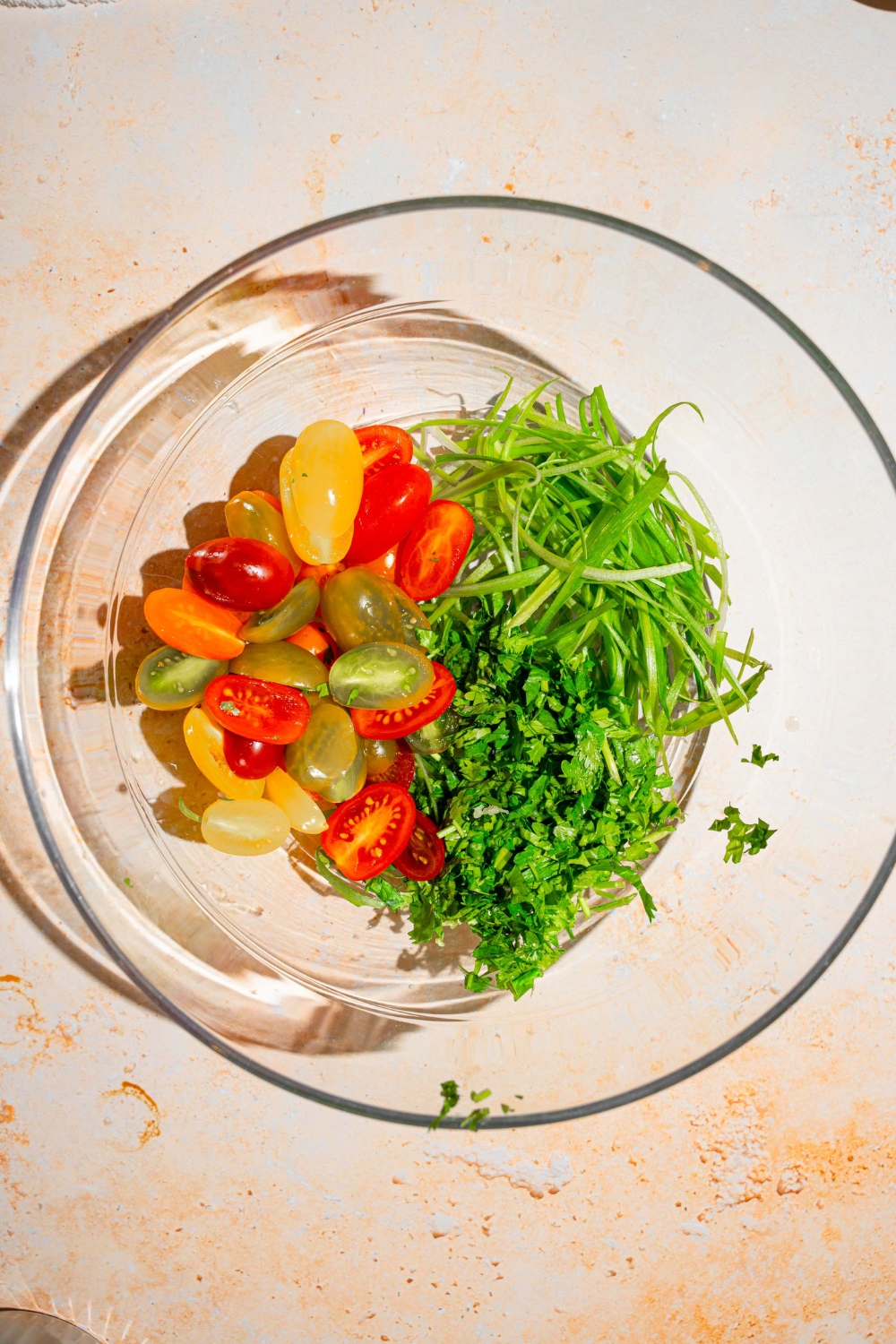 A glass bowl with sliced tomatoes, scallions, and cilantro. The bowl is on a tan counter.