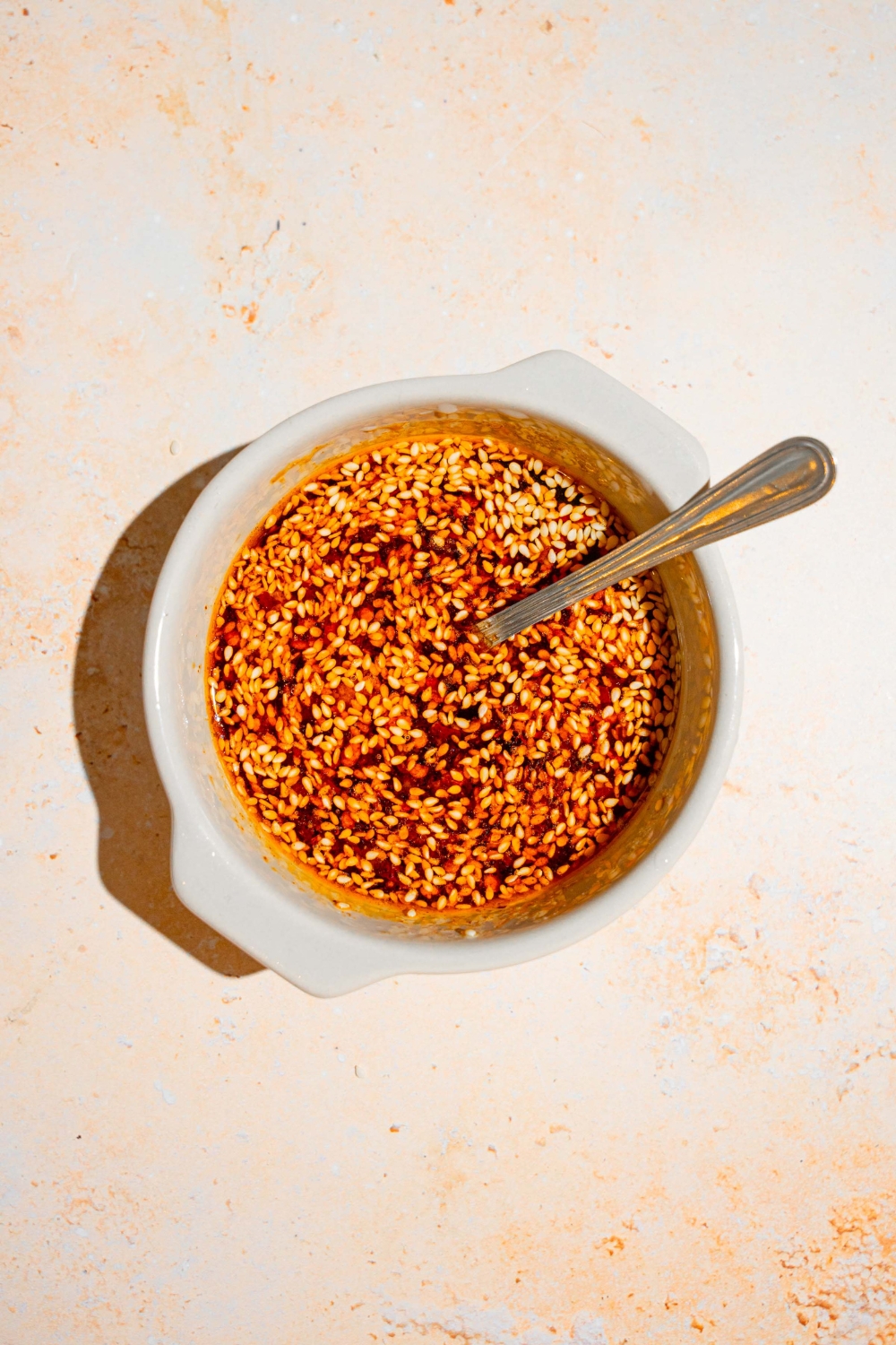 A bowl with a spoon mixing a soy sauce and chili oil dressing. The bowl is on a tan counter.