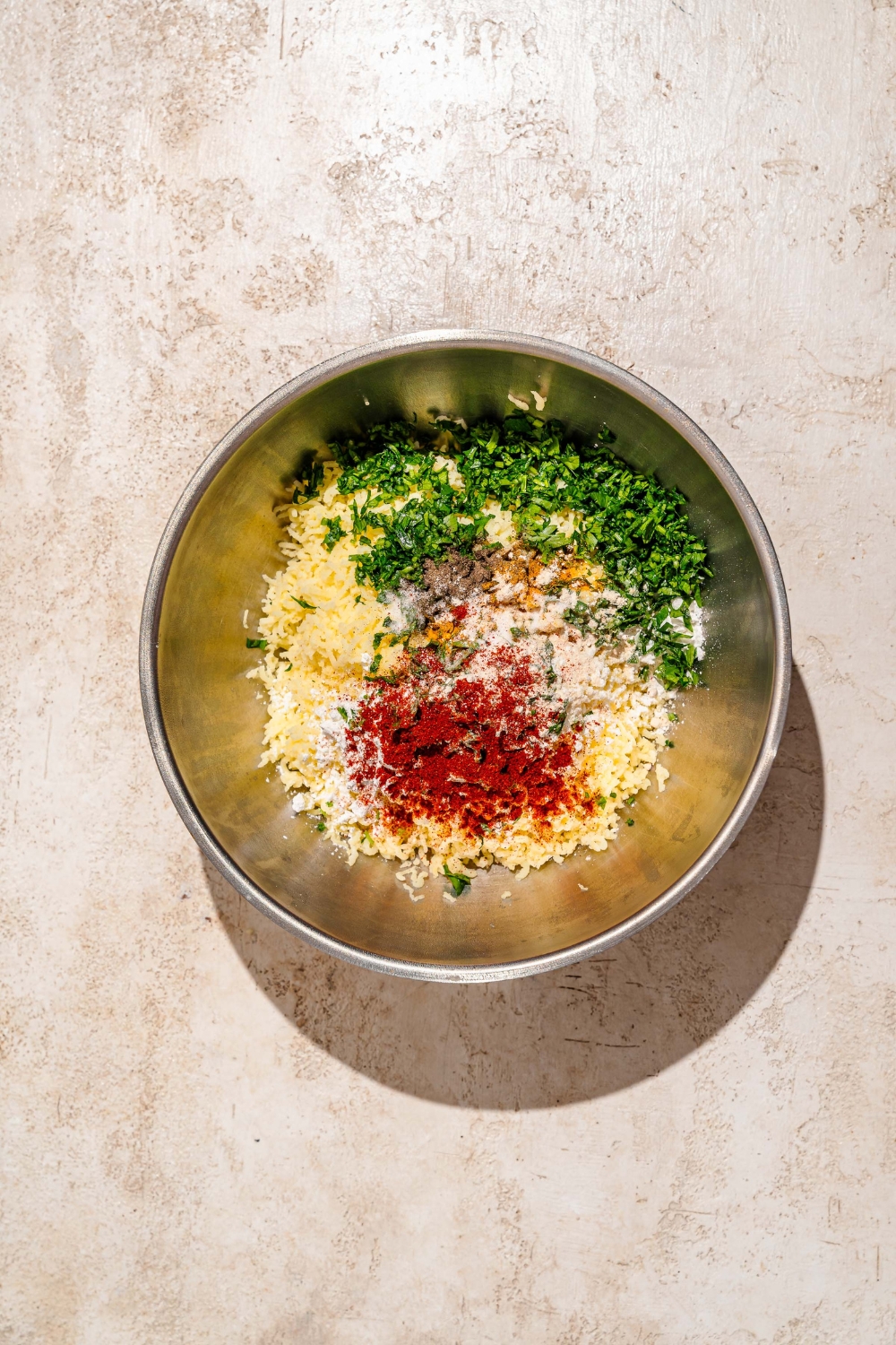 A large mixing bowl with mashed potatoes topped with seasonings including turmeric, onion powder, paprika, fresh parsley, salt and pepper.