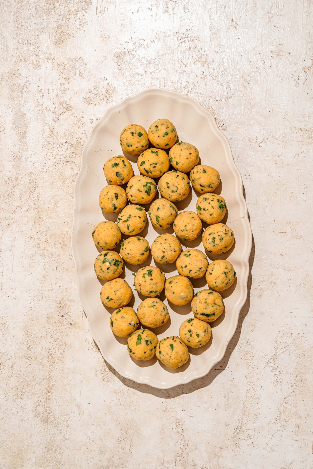 A platter with seasoned mashed potato balls. The platter is on a tan counter.