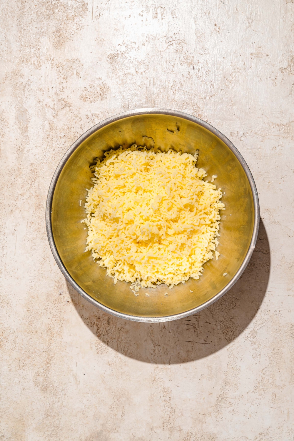A large bowl with shredded potatoes. The bowl is on a tan counter.