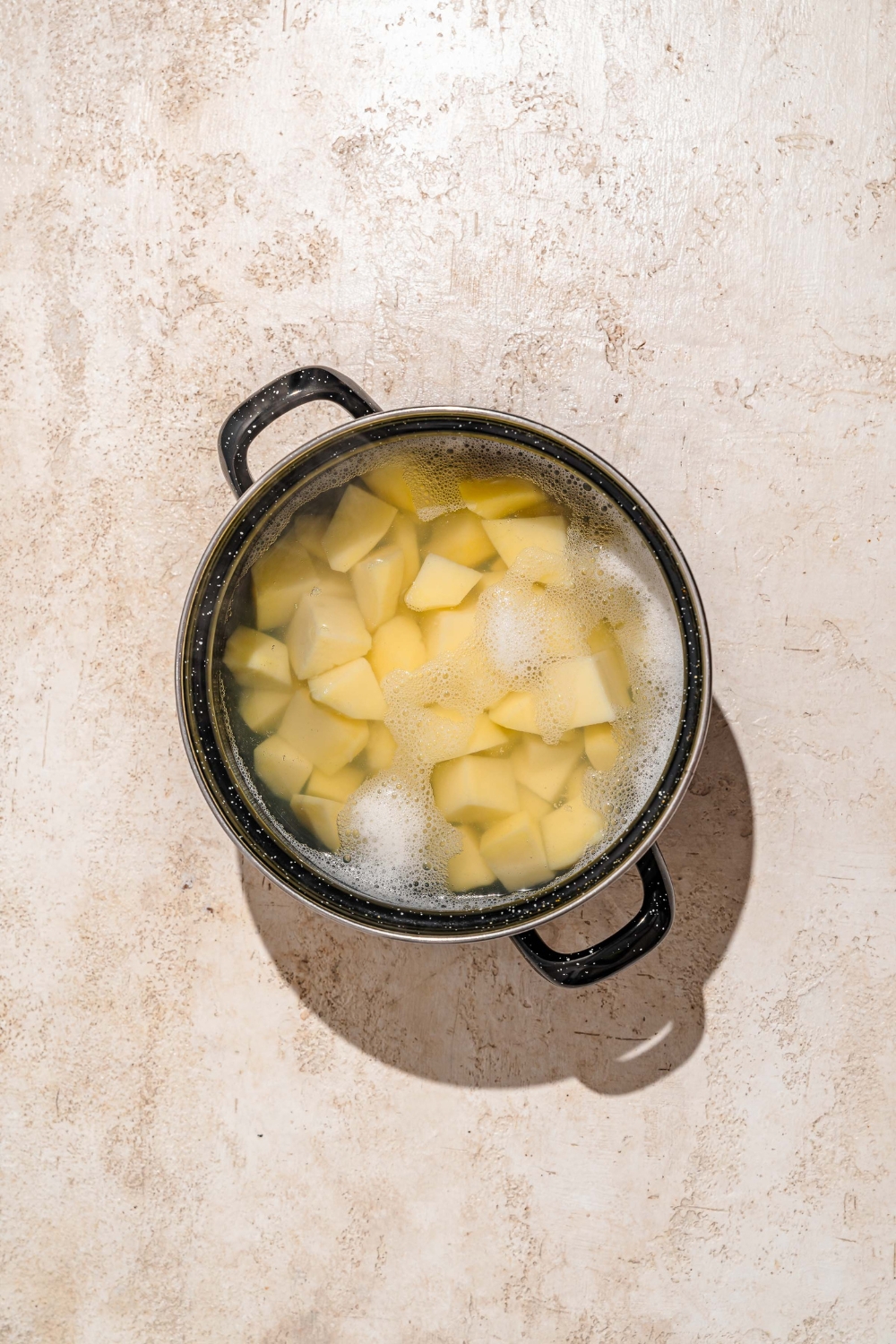 A large pot with cubed potatoes cooking in water. The pot is on a tan counter.