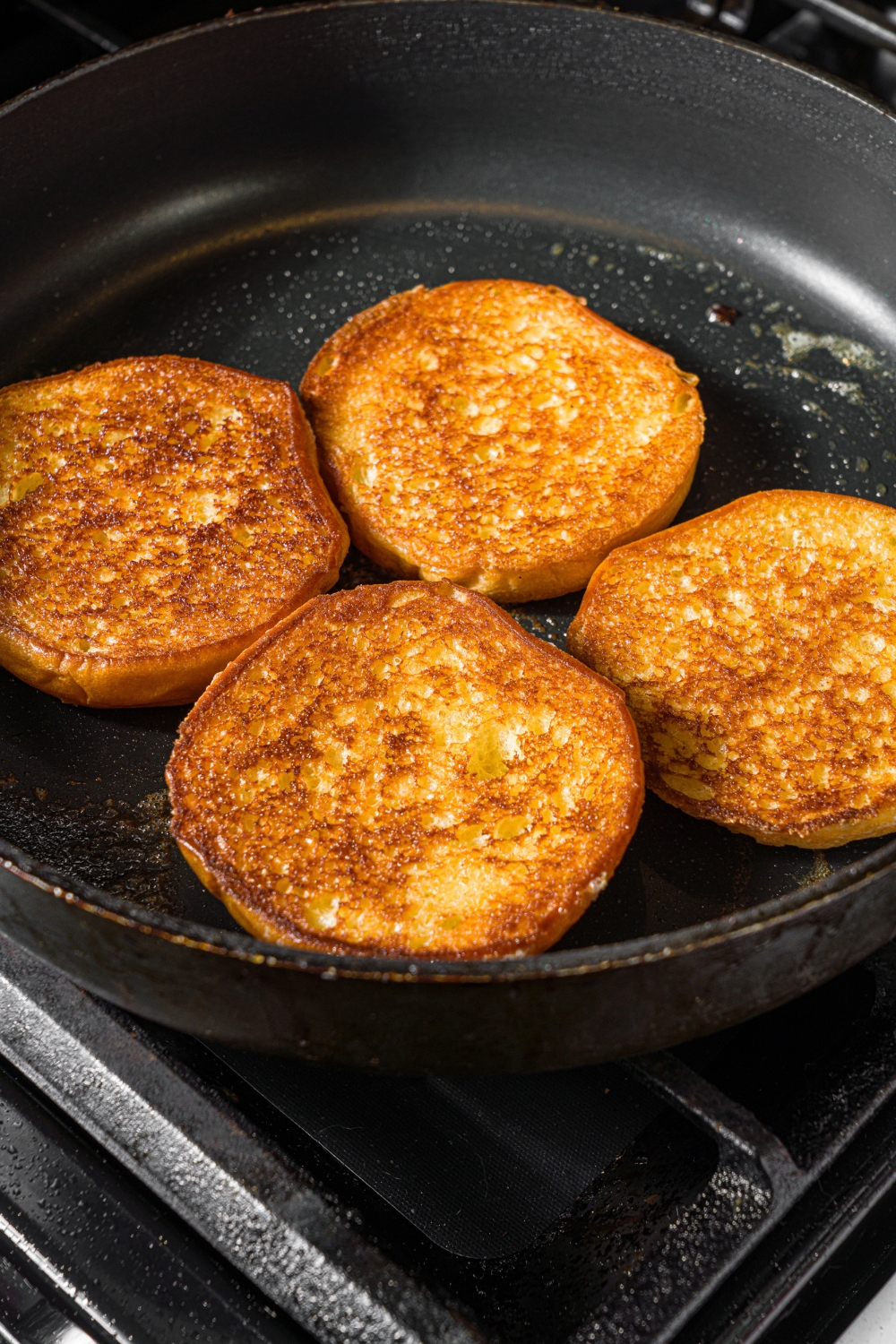A skillet with two open burger buns toasting in butter. The skillet is on the stove.