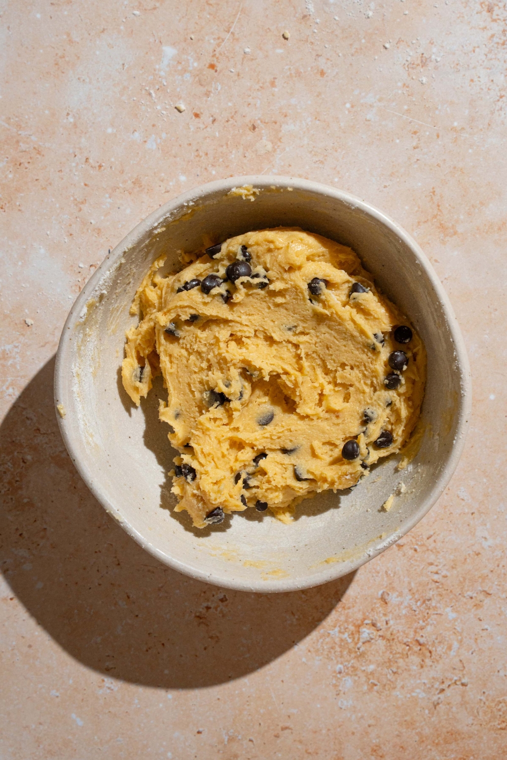 A bowl of chocolate chip cookie dough. The bowl is on a tan counter.