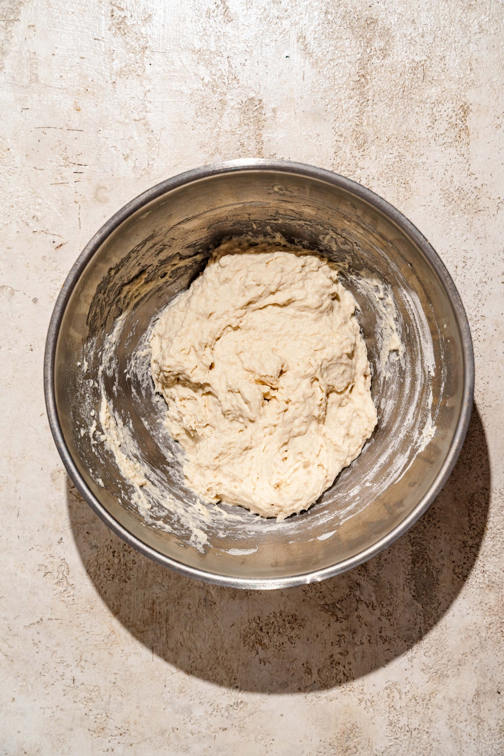 A large bowl with mixed focaccia dough. The bowl is on a tan counter.