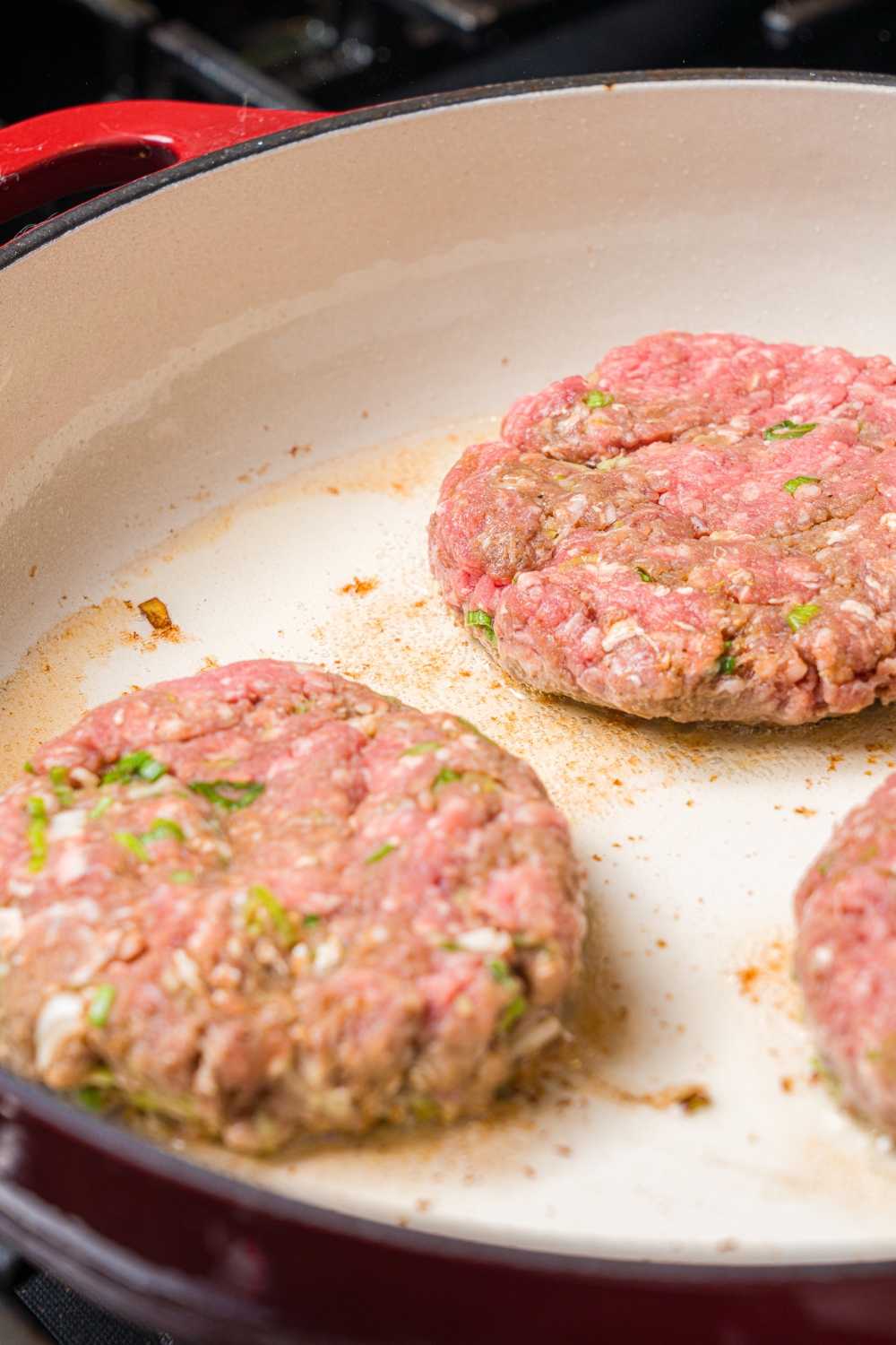 A cast iron skillet with searing hamburger steak patties.