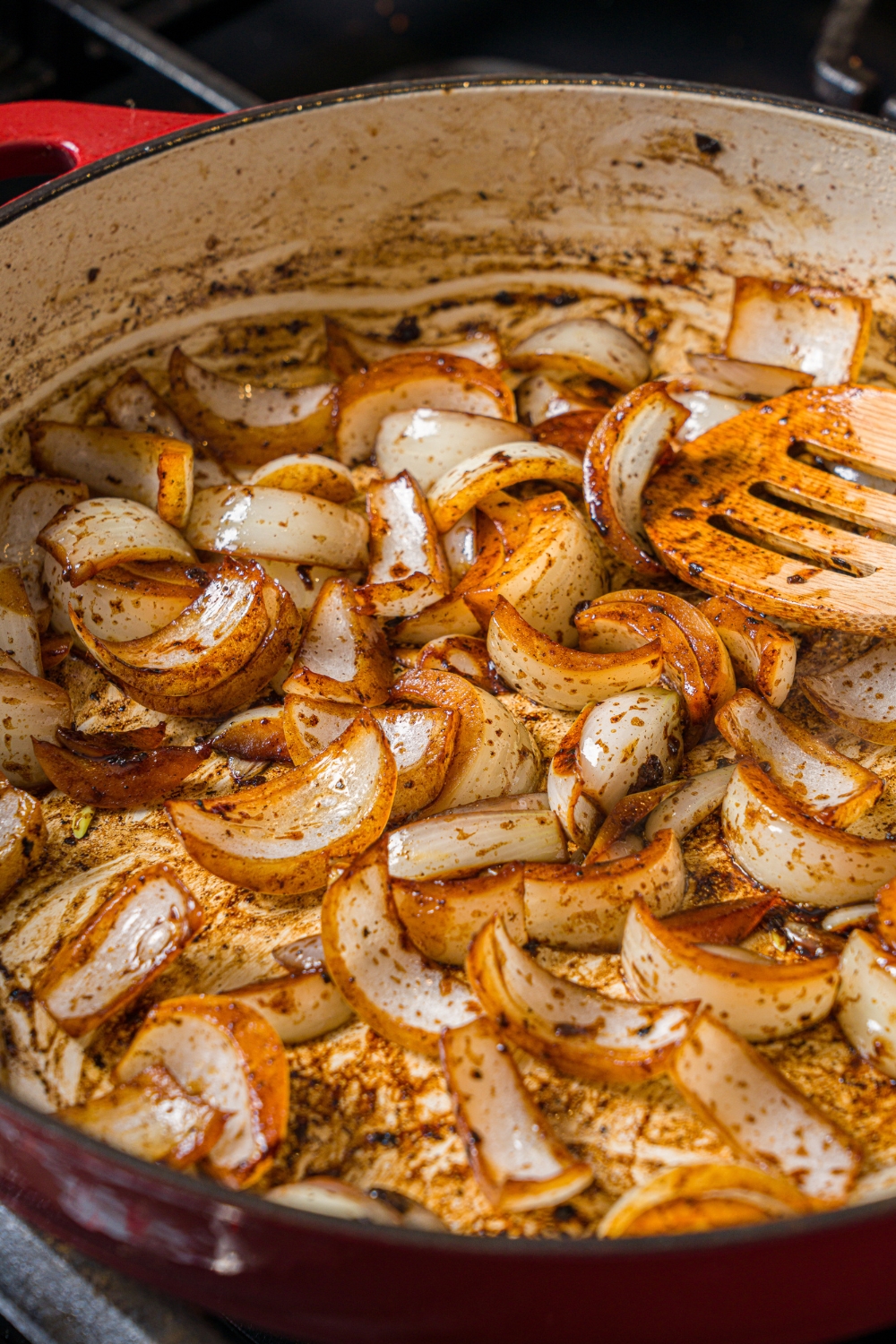 A cast iron skillet with cooked onions. The skillet is cooking on a stove.