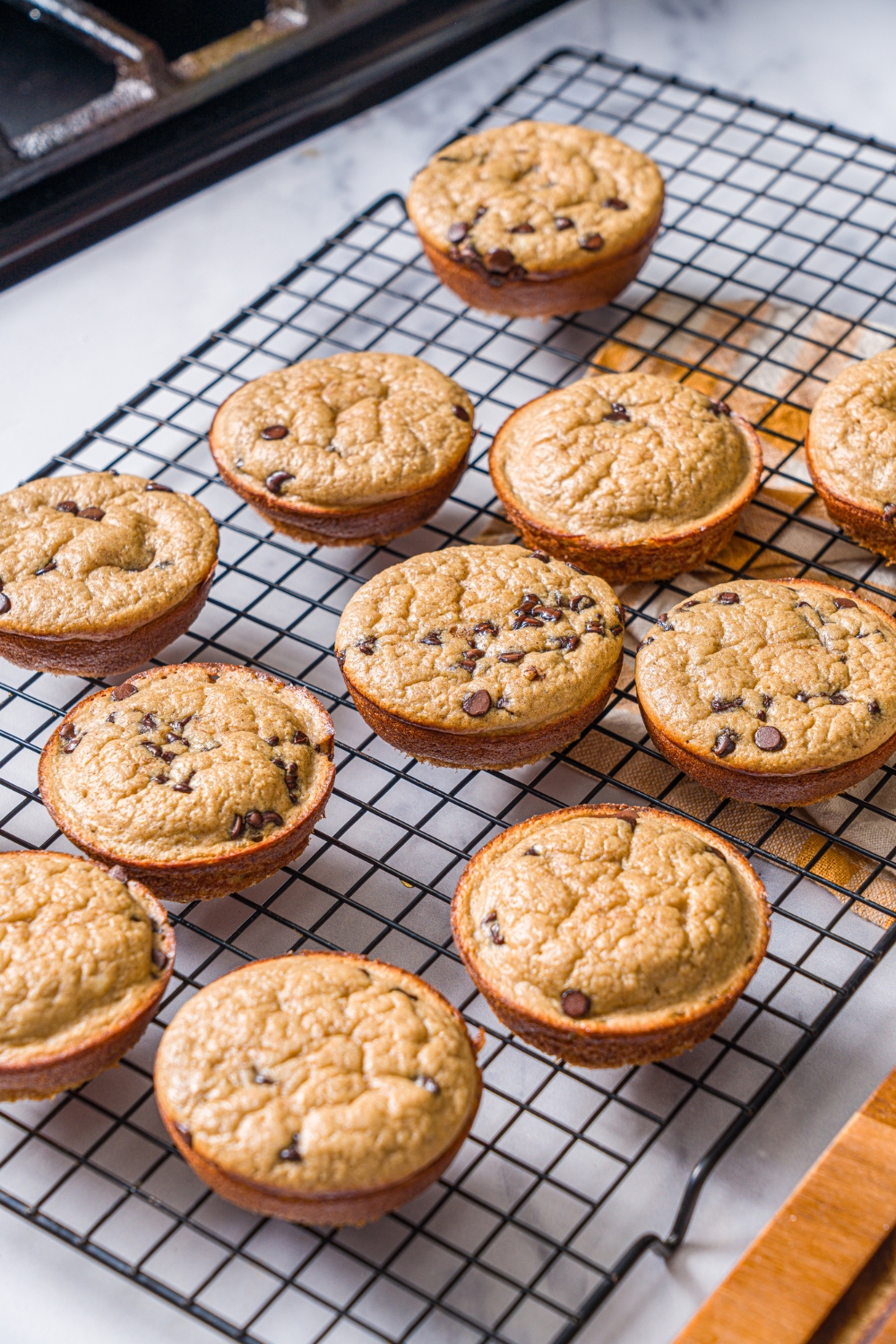 A wire rack with baked protein banana muffins. The rack is on a marble counter.