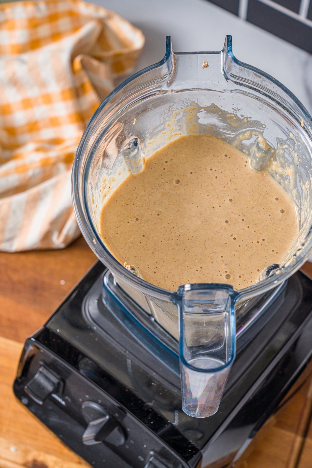 A blender with blended protein banana muffin batter. The blender is on a wooden board.