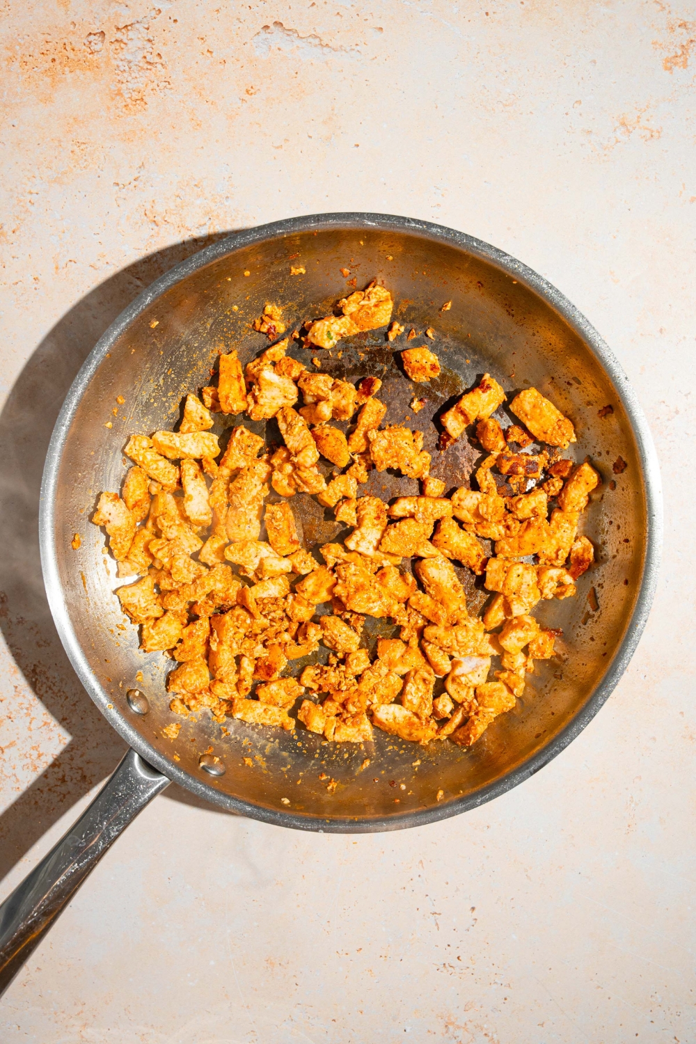 A skillet with seasoned chicken searing in oil. The skillet is on a tan counter.