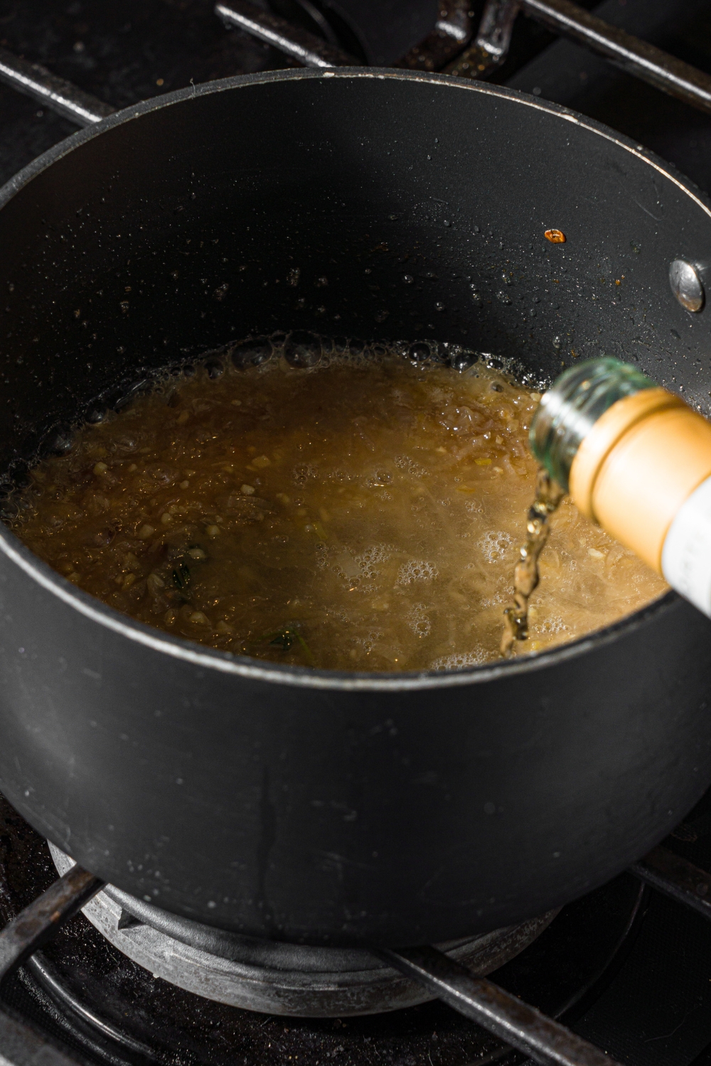 A saucepan with white wine being added to a steak frites sauce base. The saucepan is on a stove.