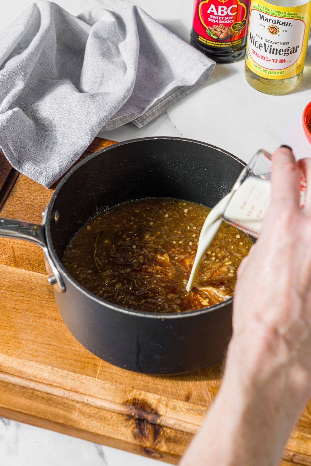 A saucepan with cream being added to a steak frites sauce mixture. The saucepan is on a wooden board.
