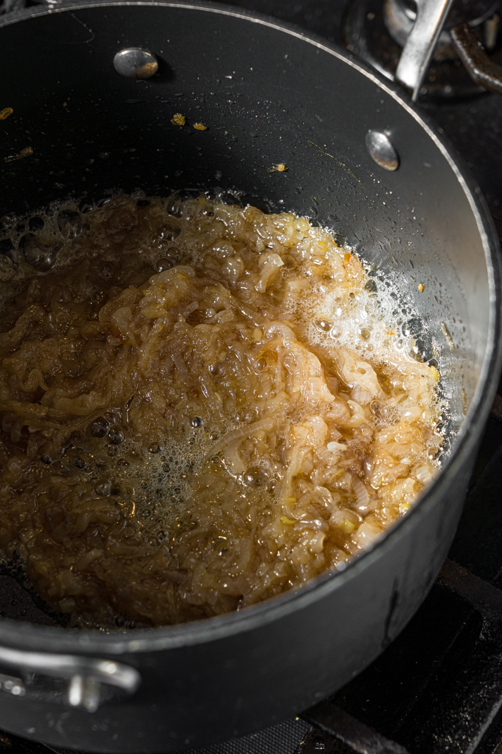 A saucepan with shallots cooking in butter. The saucepan is on a stove.