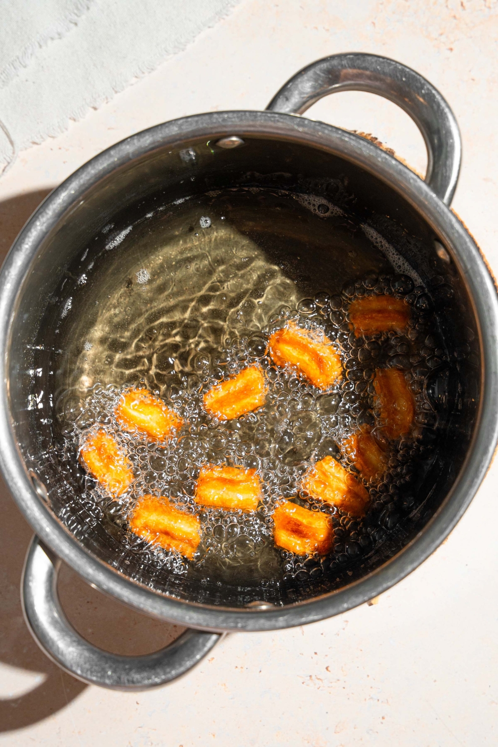 A large pot with boiling water and butter frying mini churros. The pot is on a tan counter.