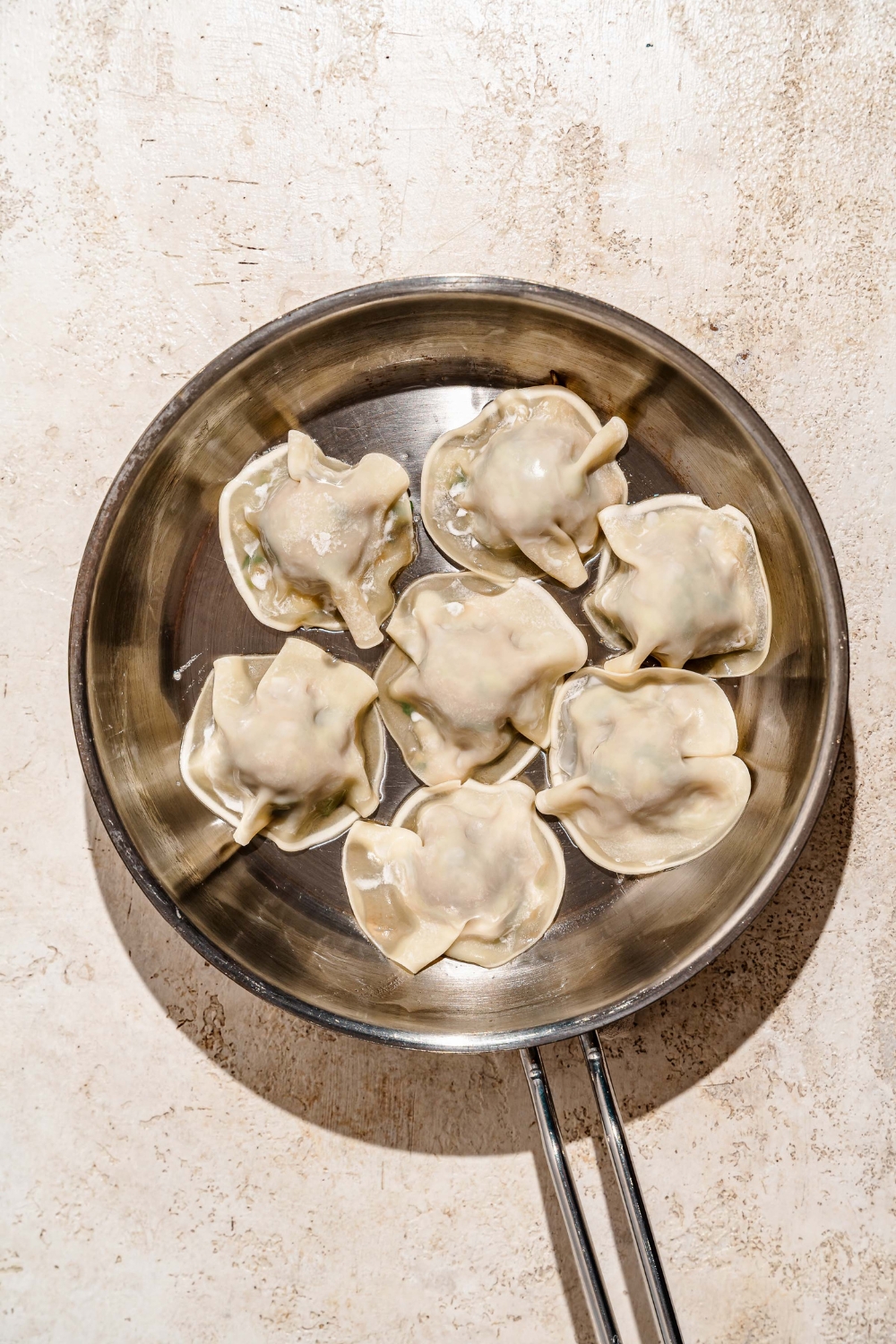 A skillet with uncooked pork and shrimp dumplings. The skillet is on a tan counter.