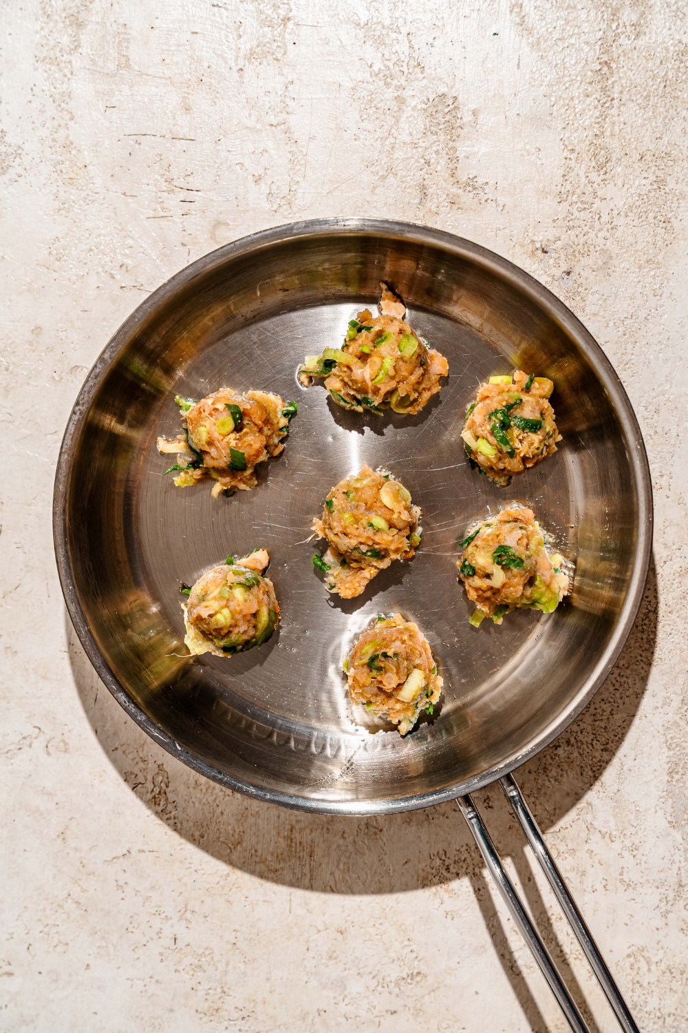 A skillet with several balls of pork and shrimp dumpling mixture. The skillet is on a tan counter.