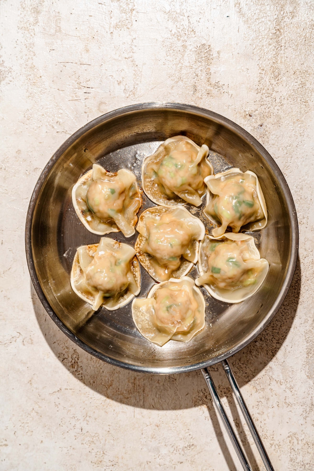 A skillet with fried pork and shrimp dumplings. The skillet is on a tan counter.