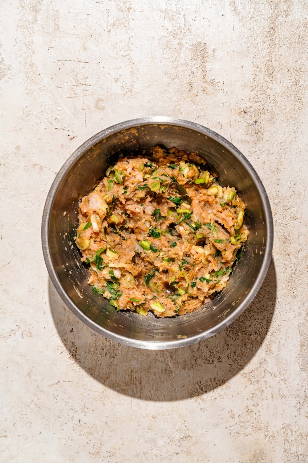 A large bowl with a pork and shrimp dumpling mixture. The bowl is on a tan counter.