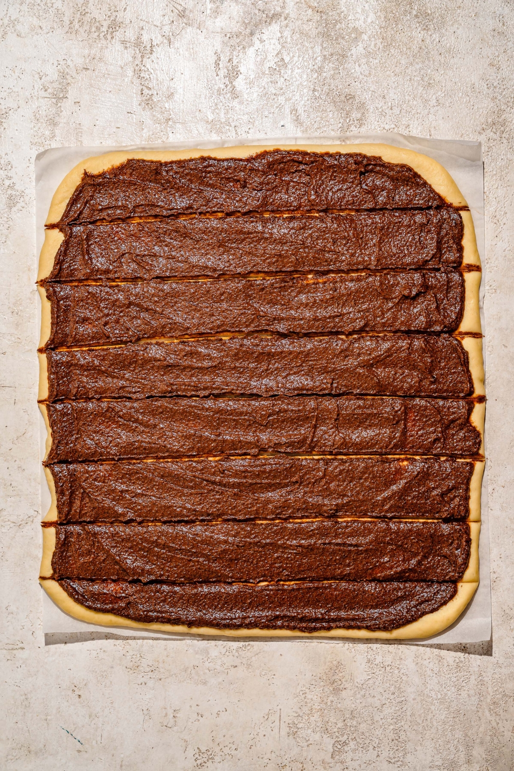 A tan counter with a rolled out rectangle of sticky bun dough topped with caramel mixture and sliced in several rows.