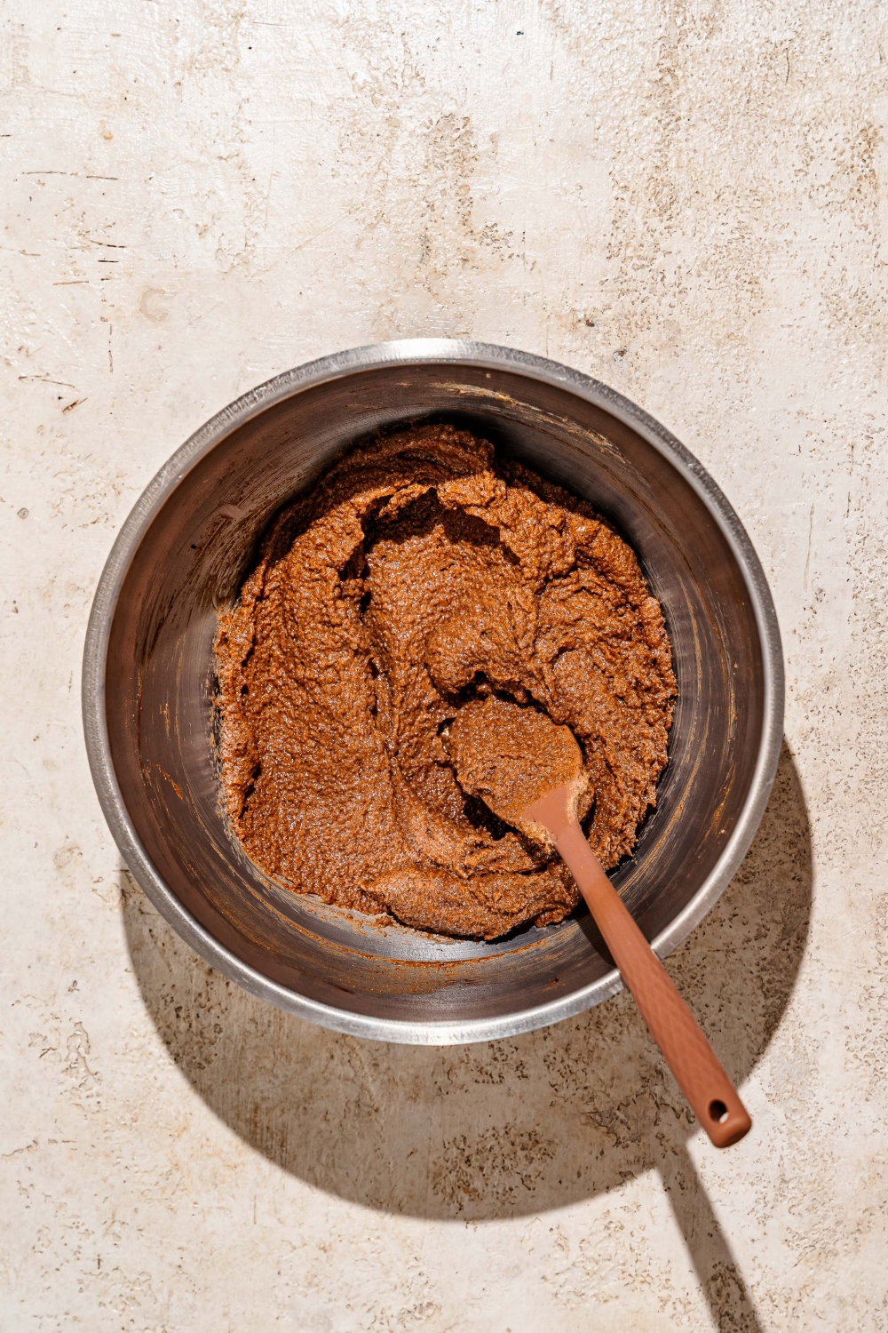 A large mixing bowl with a wooden spoon mixing a caramel filling mixture. The bowl is on a tan counter.