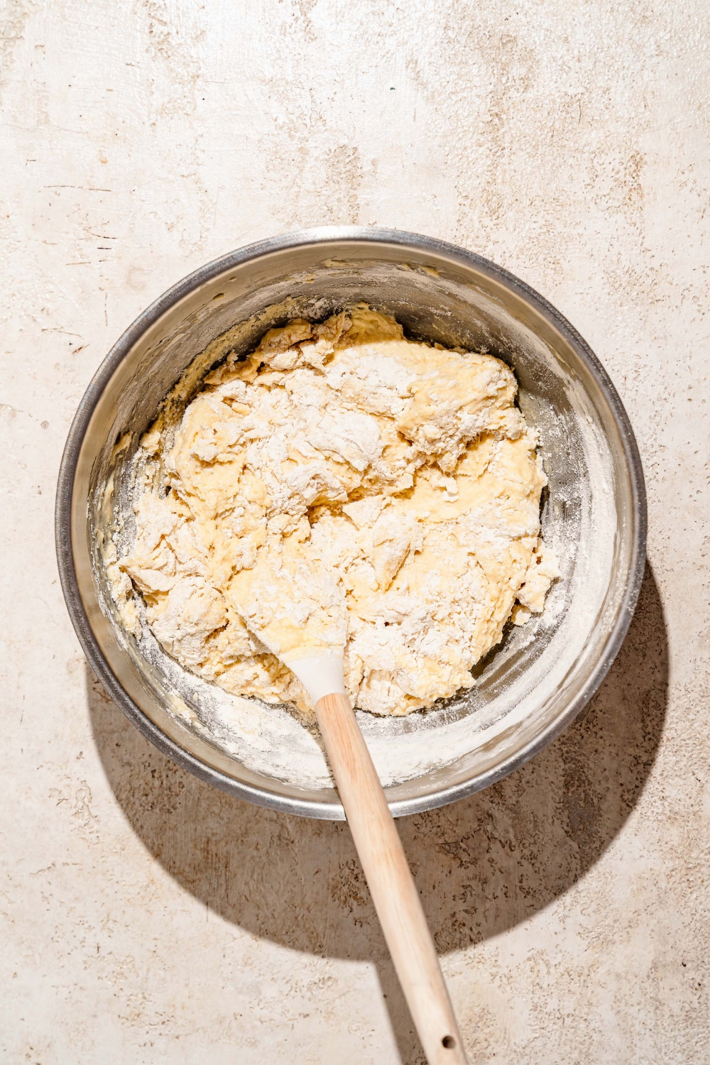 A large bowl with a wooden spoon mixing ingredients to make sticky bun dough. The bowl is on a tan counter.