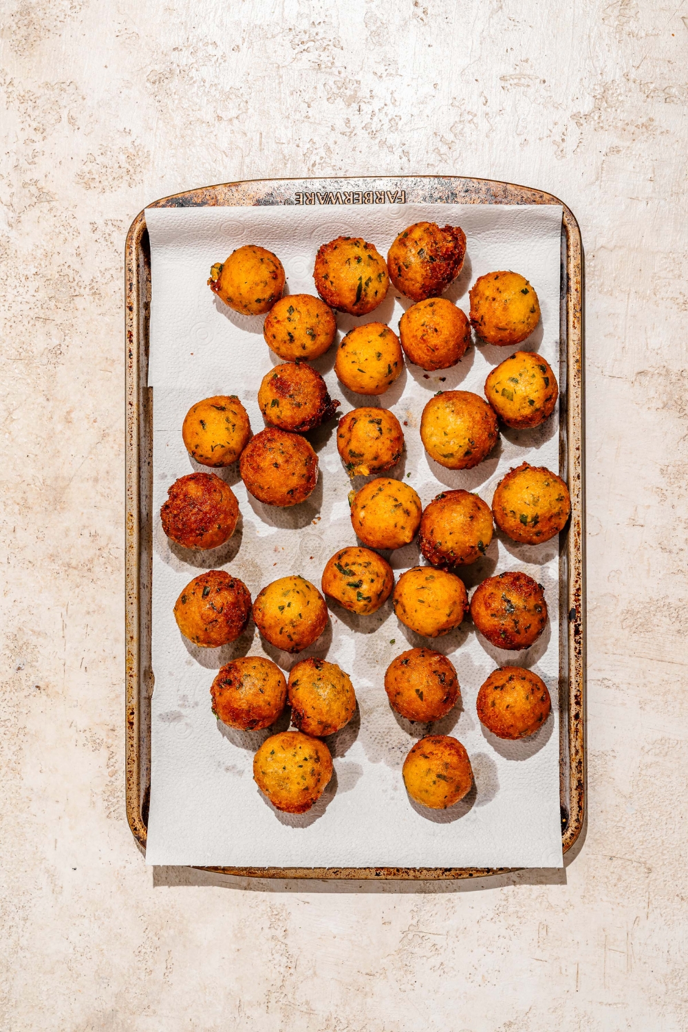 A baking sheet lined with parchment paper with crispy potato balls. The sheet is on a tan counter.