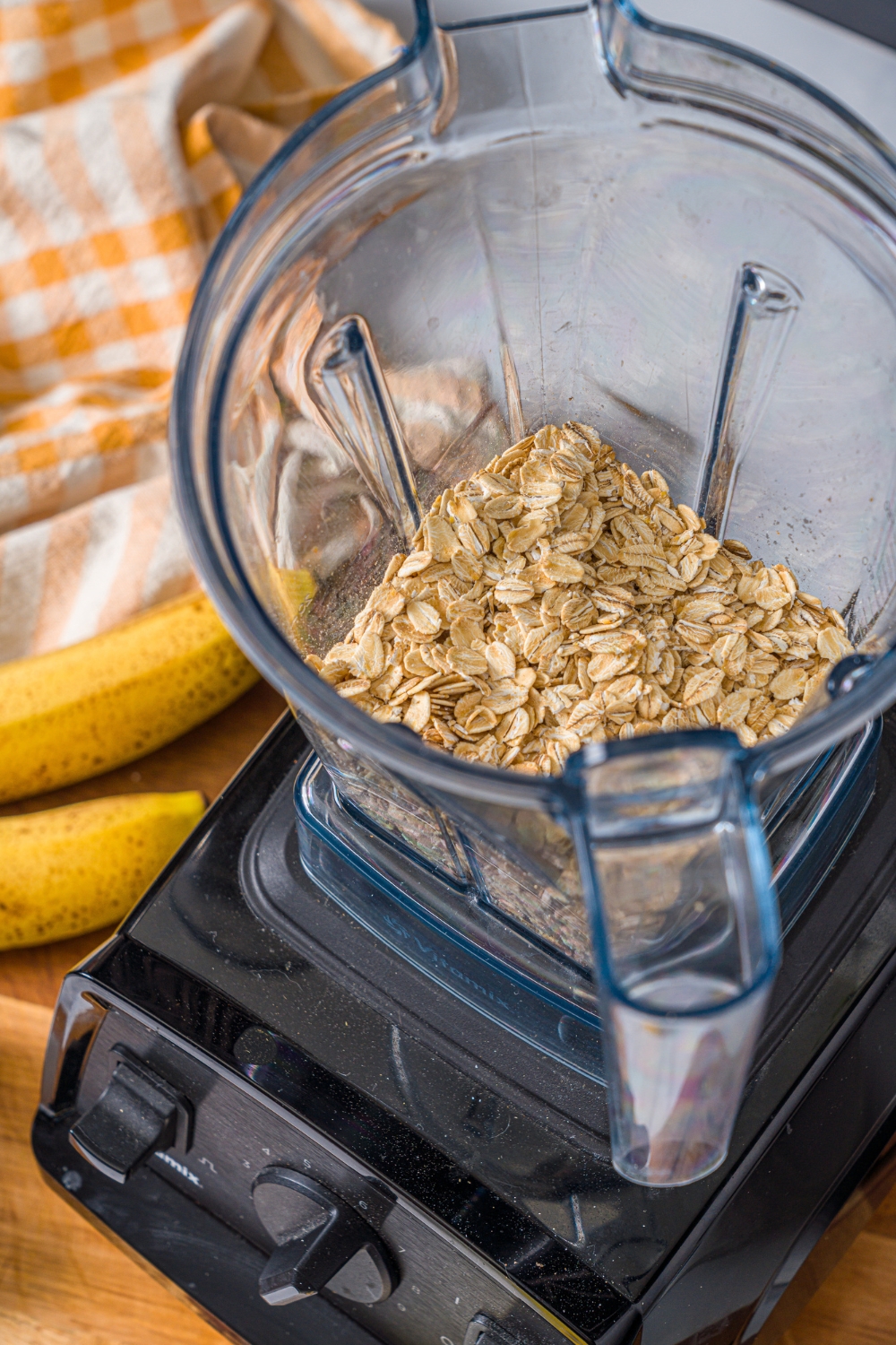 A blender with rolled oats. The blender is on a wooden board.